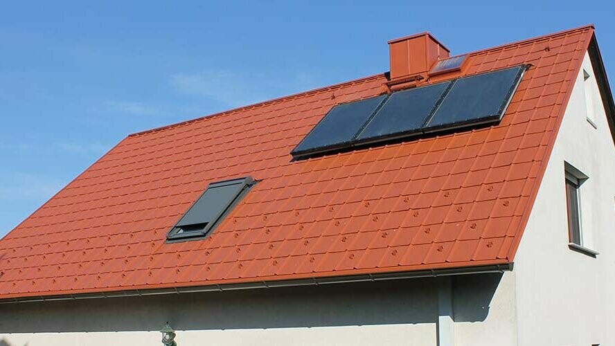 Maison individuelle avec toit à deux versants recouvert de tuiles PREFA rouge tuile. Surface de toit avec installation solaire et fenêtre de toit
