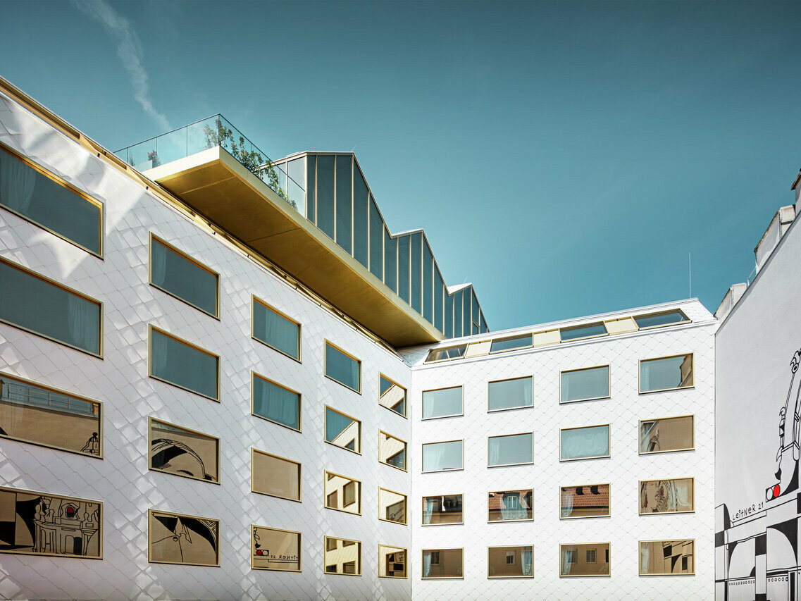 Vue en perspective de l'hôtel "THE ROCK Radisson RED Vienna" à Vienne, caractérisé par sa façade innovante en aluminium PREFA avec des losanges de toit et de mur 44 × 44 en P.10 blanc pur. Les fenêtres à vitrage miroir, disposées de manière irrégulière, reflètent l'environnement de manière dynamique.