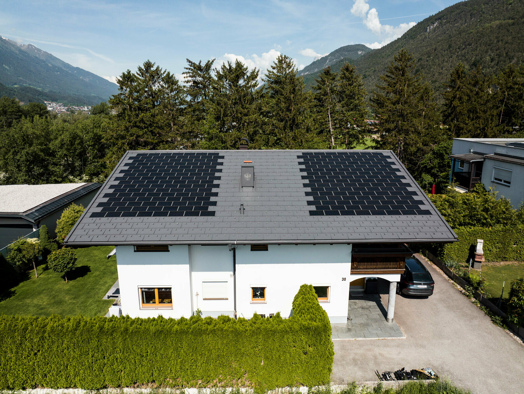La photo montre une maison individuelle recouverte avec la tuile solaire PREFA petit format et le R.16 couleur P.10 gris sombre dans un environnement rural.