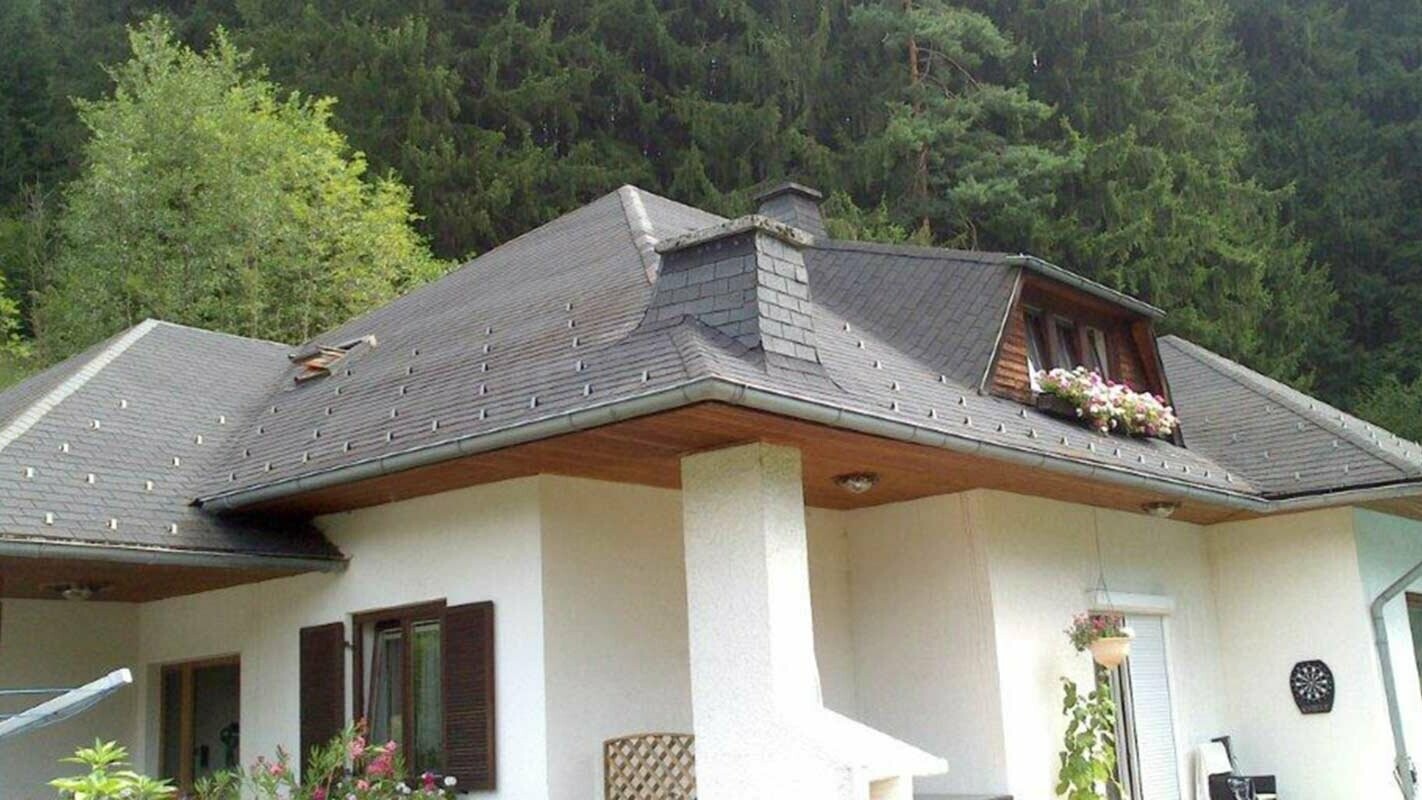 Maison individuelle avec toit à croupes avant la rénovation de toiture à l’aide de tuiles PREFA, lucarne en forme de trapèze incluse
