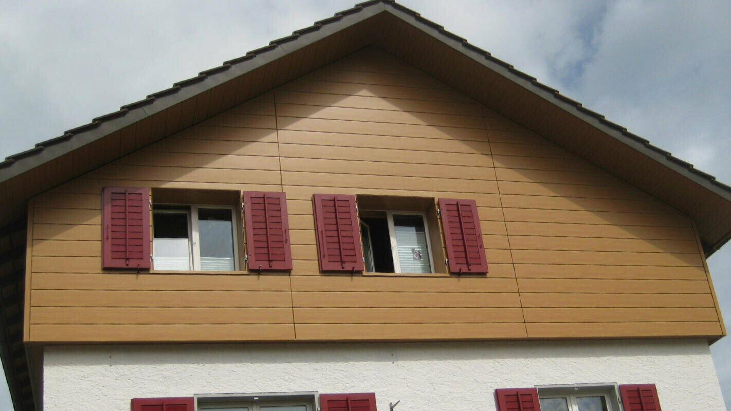 Façade imitation bois avec Sidings PREFA, pose à l’horizontale, fenêtres avec volets rouges
