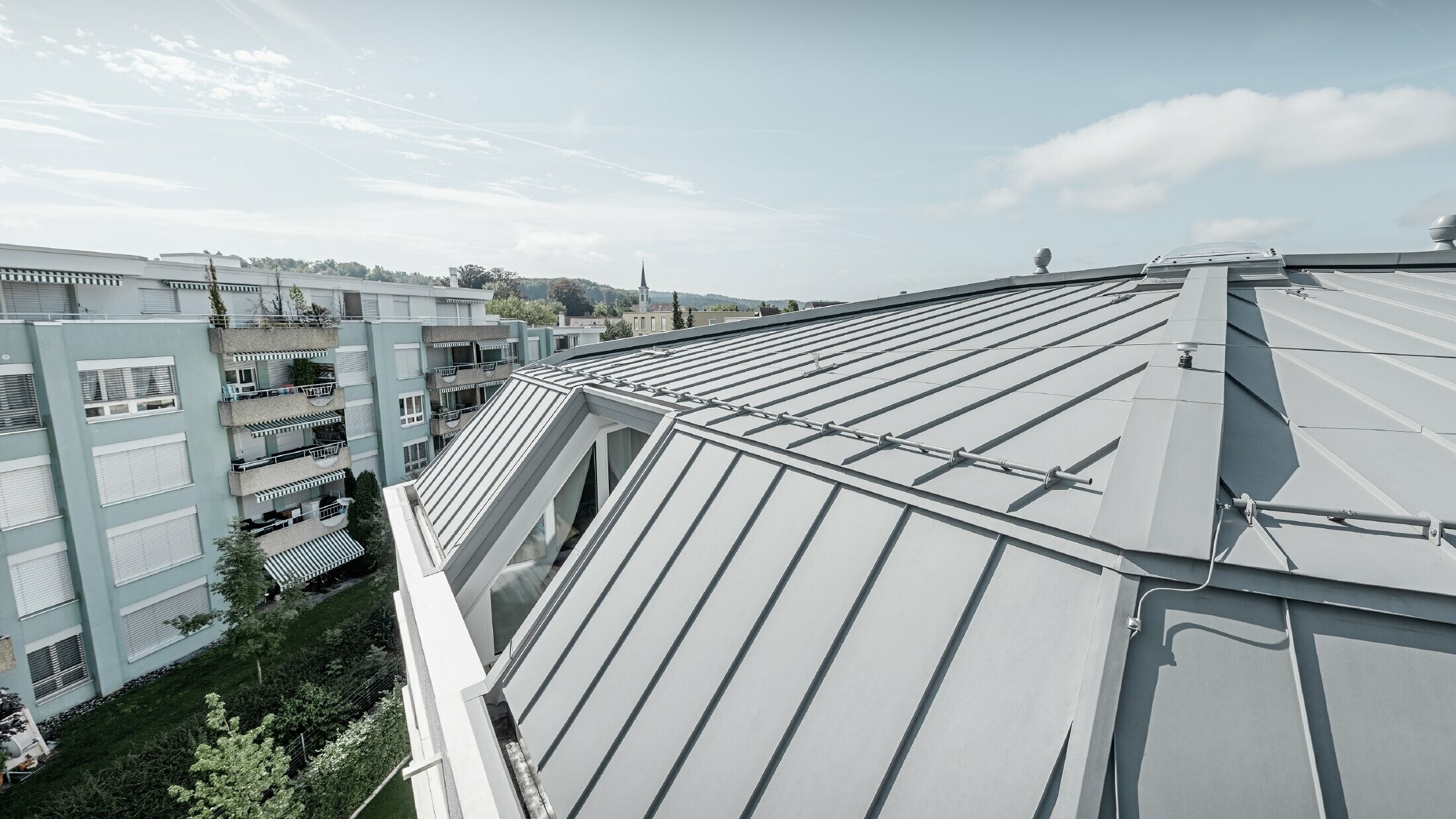 Vue détaillée de la surface de toiture d’un immeuble collectif ; toit à joint debout réalisé avec Prefalz PREFA couleur gris quartz.