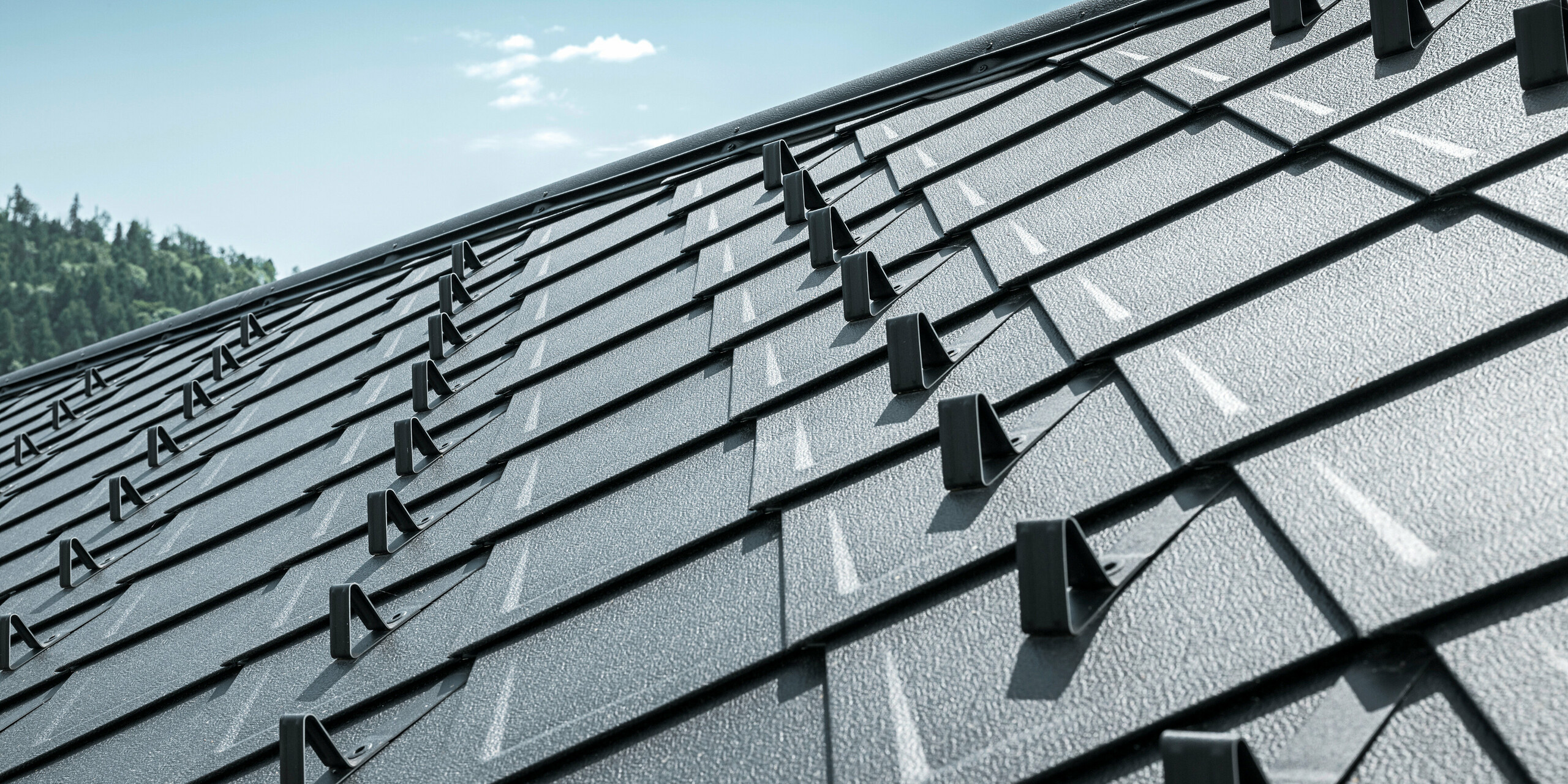 Gros plan du toit d'une maison familiale traditionnelle à Stara Bystrica, en Slovaquie, recouvert d'une toiture durable en losanges 29 × 29 de couleur P.10 noir. La couverture en aluminium durable au look élégant est dotée de pare-neige intégrés qui offrent une sécurité supplémentaire. La structure claire et le design moderne des losanges du toit confèrent au bâtiment un aspect général harmonieux et esthétique.