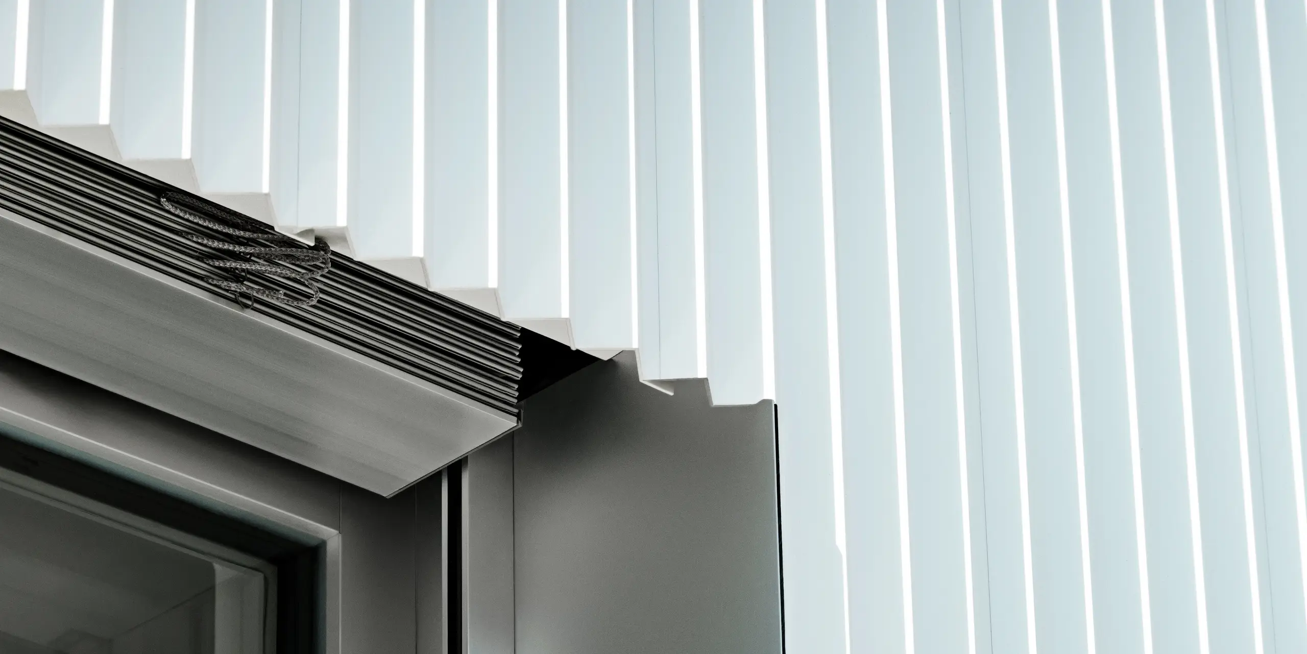 Gros plan précis d'un encadrement de fenêtre avec profilé triangle PREFA P.10 Blanc Pur. Les profilés en aluminium aux contours nets épousent parfaitement la fenêtre, complétée par des guides extérieurs intégrés pour stores vénitiens. La finition haut de gamme témoigne du savoir-faire irréprochable, de la durabilité et de la résistance aux intempéries des systèmes de façade PREFA – idéaux pour une architecture moderne et raffinée.