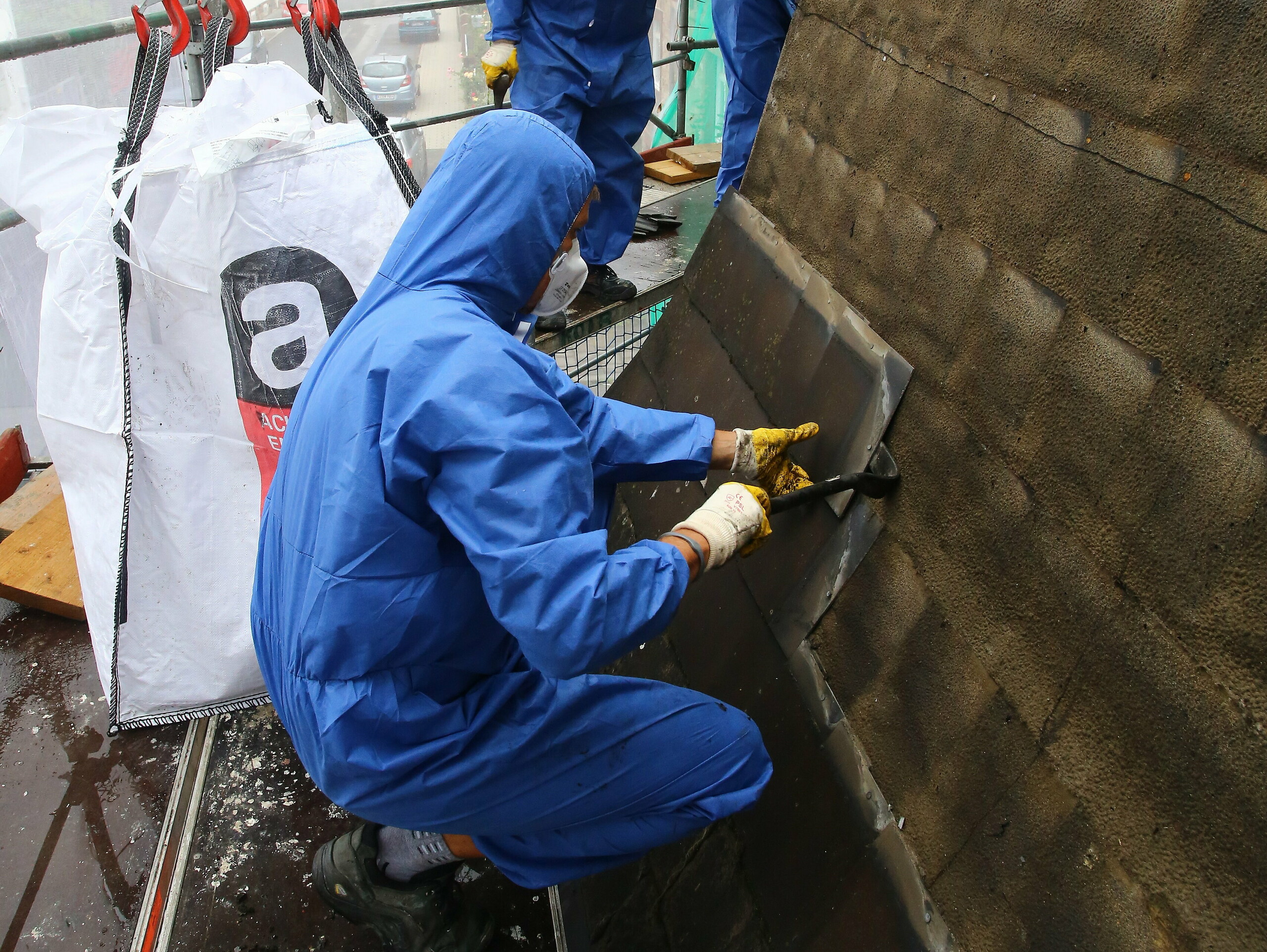 Un artisan spécialisé en train de démonter et d’éliminer une vieille couverture de toit amiantée avec un masque de protection respiratoire contre la poussière d’amiante