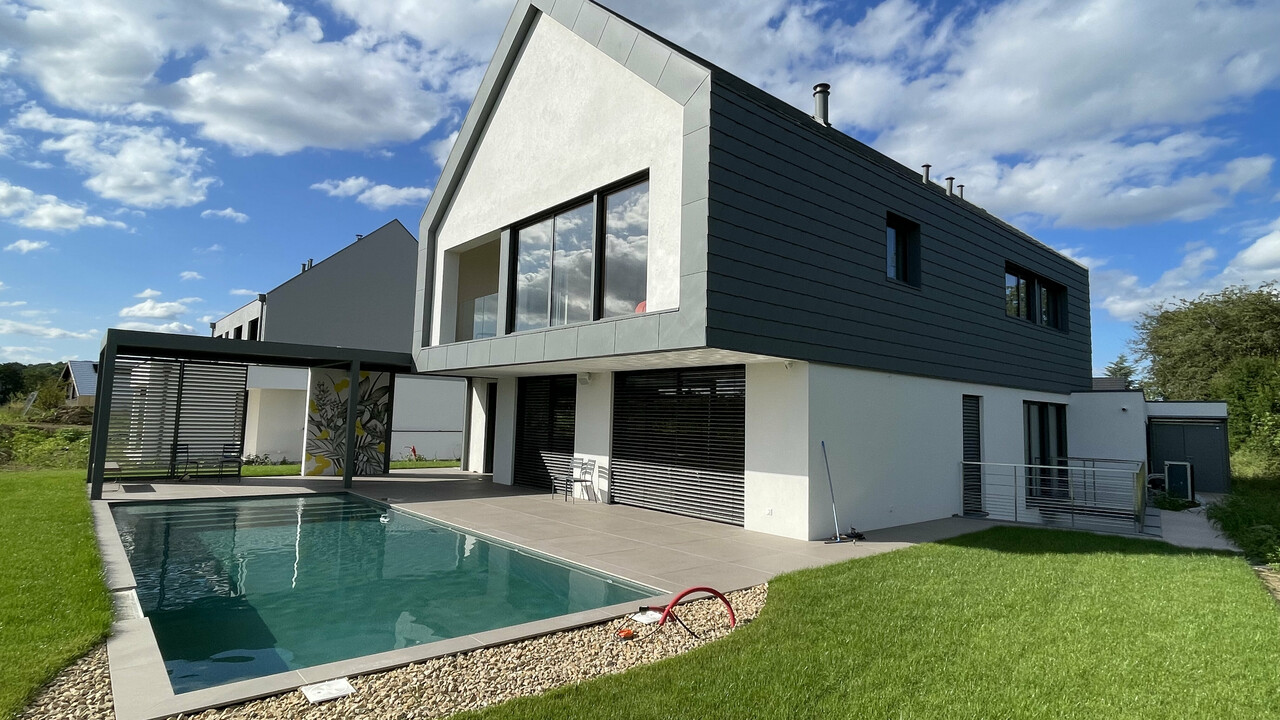 Vue d'ensemble de cette nouvelle maison individuelle dont la toiture et la façade contemporaine ont été recouvertes de bardeaux en aluminium PREFA. On aperçoit une jolie piscine en premier plan.