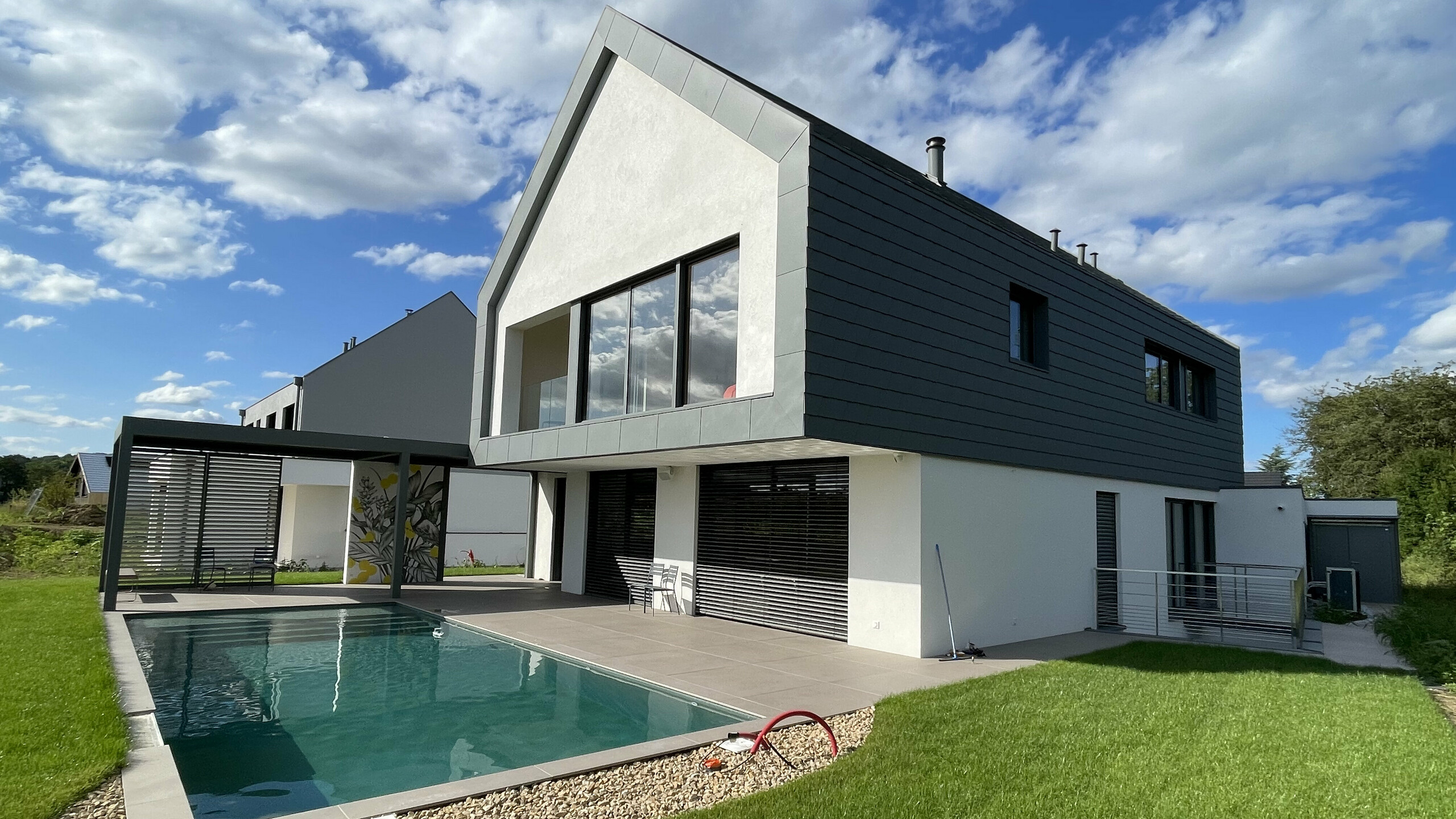 Vue d'ensemble de cette nouvelle maison individuelle dont la toiture et la façade contemporaine ont été recouvertes de bardeaux en aluminium PREFA. On aperçoit une jolie piscine en premier plan.