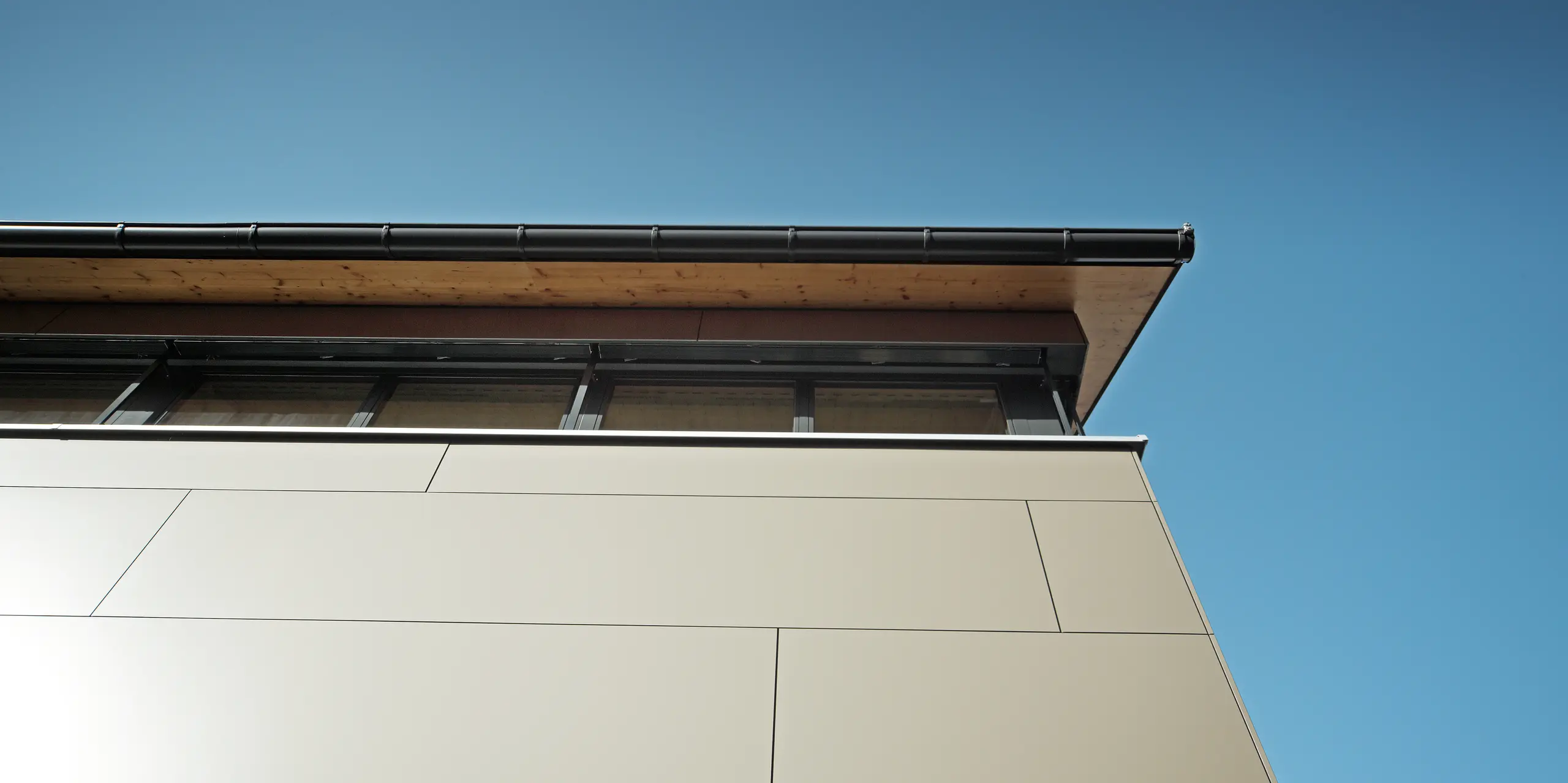 Detailaufnahme der Fassade eines Einfamilienhauses in Hohenems, ausgestattet mit PREFA Aluminium Verbundplatten in Bronzemetallic. Die präzise Montage zeigt keine sichtbaren Befestigungselemente, was die glatte und homogene Oberfläche betont. Die hochwertigen, korrosionsbeständigen Platten bieten durch ihre robuste Beschaffenheit und Farbbeständigkeit einen langlebigen Schutz und verleihen dem Haus eine moderne und einzigartige Optik.