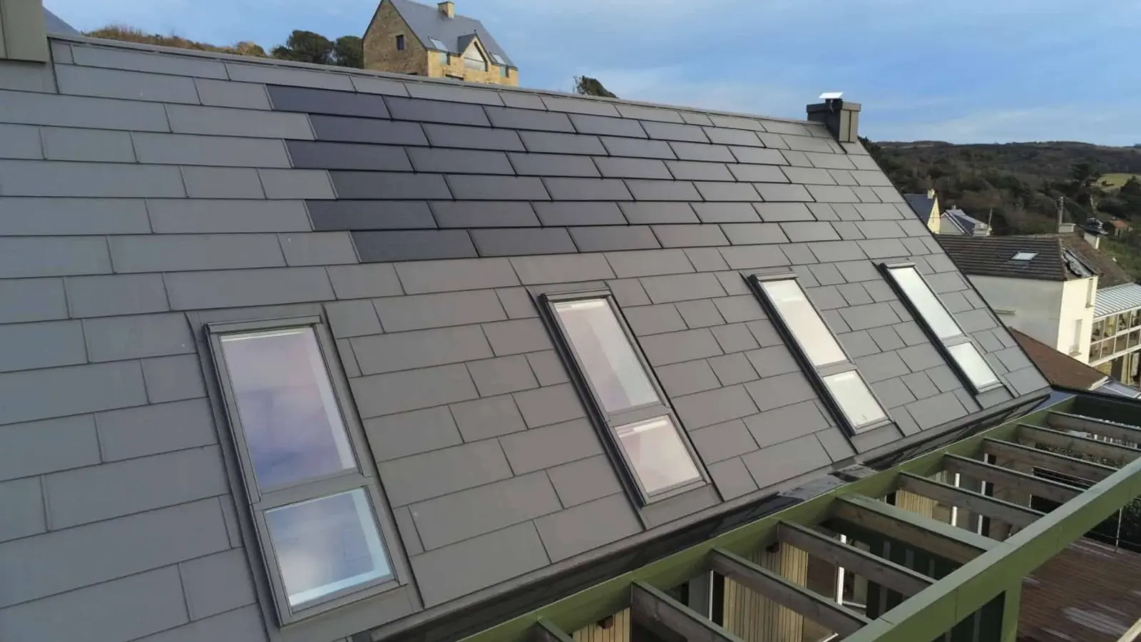 Vue latérale depuis la toiture de cette maison individuelle située face à la mer, à Les Pieux. Elle a récemment été rénovée avec les produits de toiture PREFA : panneaux FX.12 et tuile solaire PREFA dans la teinte P.10 gris sombre.
