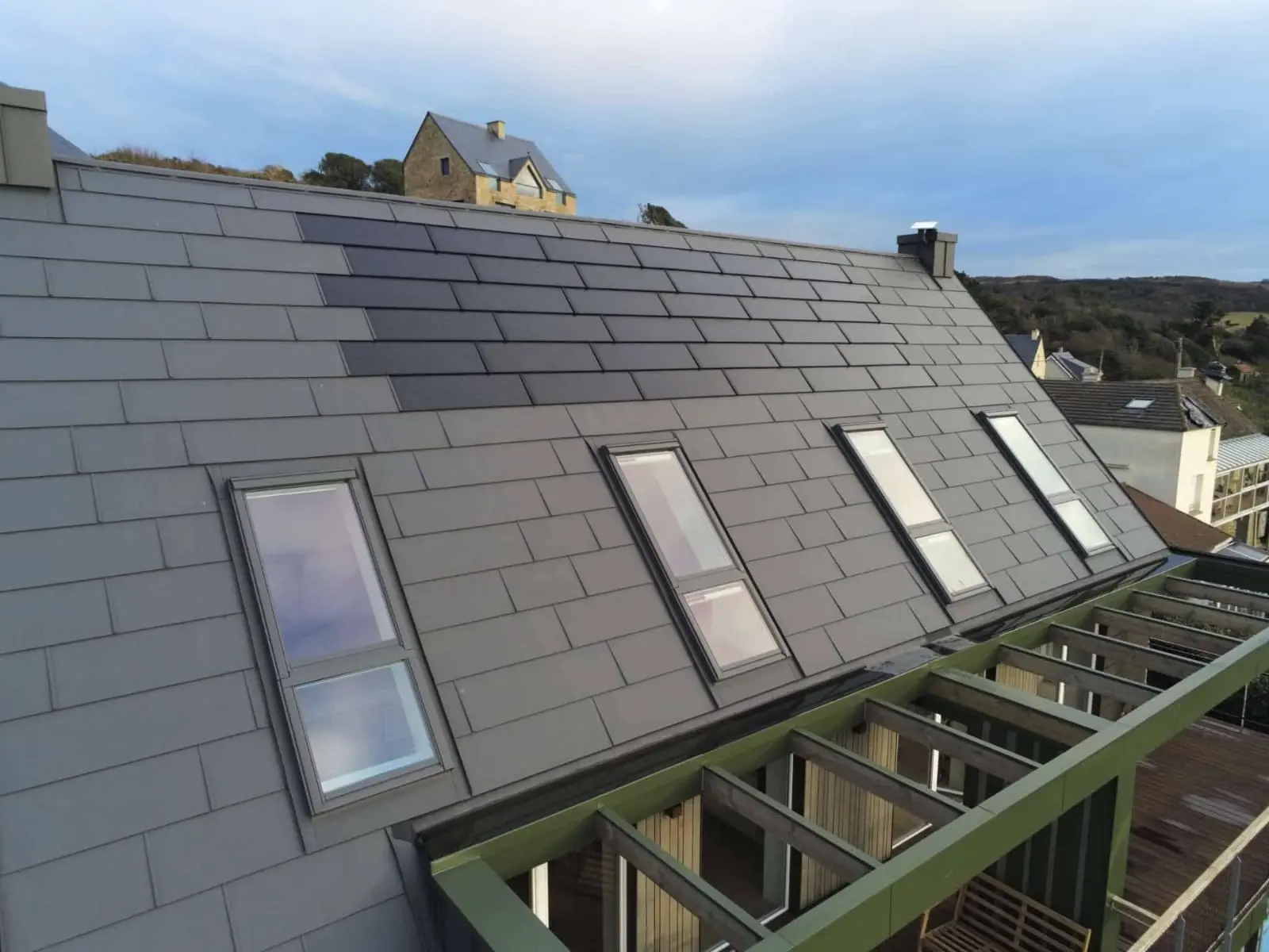 Vue latérale depuis la toiture de cette maison individuelle située face à la mer, à Les Pieux. Elle a récemment été rénovée avec les produits de toiture PREFA : panneaux FX.12 et tuile solaire PREFA dans la teinte P.10 gris sombre.