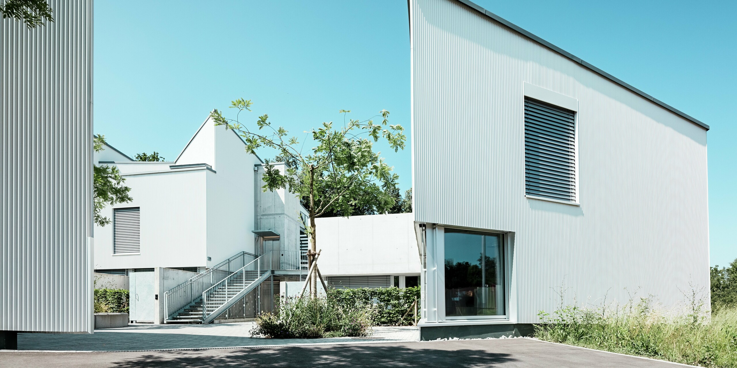 Une harmonieuse alliance entre architecture et nature : les mini-maisons modernes de Zollikerberg, dotées de profilés triangle PREFA P.10 blanc pur, présentent une silhouette structurée et résistante aux intempéries. Les formes raffinées des toitures et les lignes verticales des façades créent un aspect dynamique, tandis que le revêtement en aluminium offre une protection durable et une élégance nécessitant peu d’entretien, pour des solutions d’habitat durables.