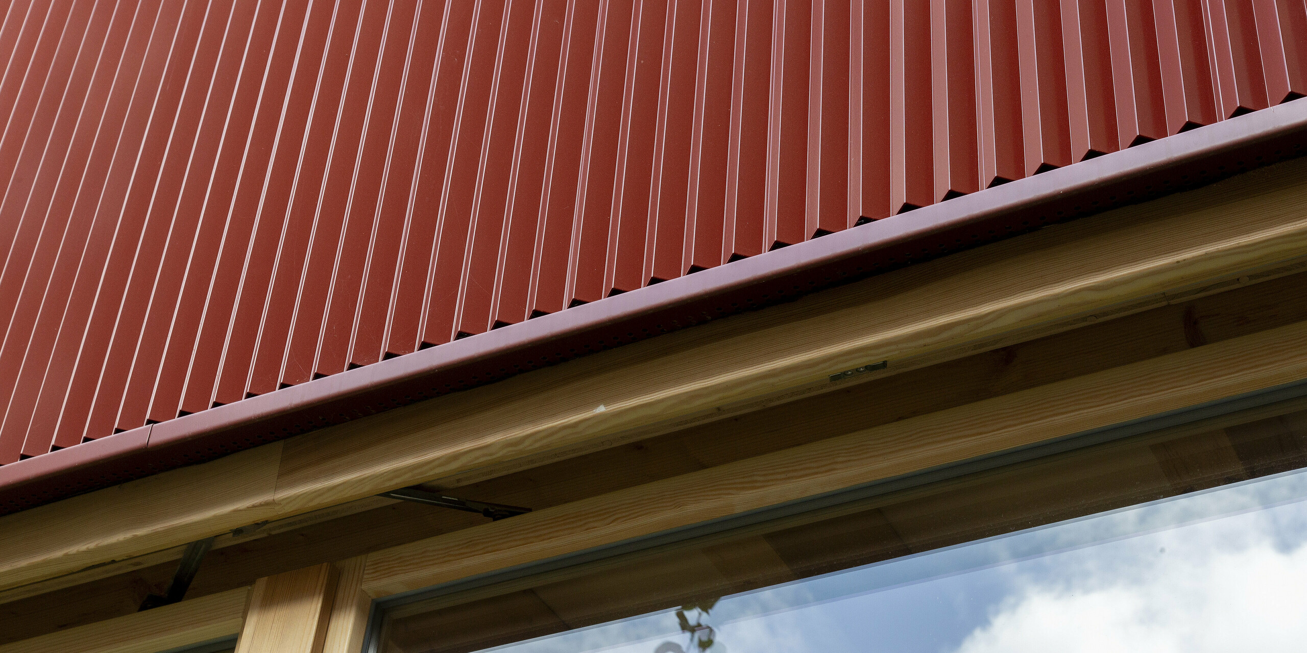 Les lignes épurées du profil triangle PREFA en coloris rouge oxyde dominent la façade minimaliste. Les nervures verticales créent un jeu de lumière saisissant qui souligne la modernité du design. Associé à la chaleur du bois et aux généreuses surfaces vitrées, ce procédé aboutit à un concept à la fois durable et élégant.