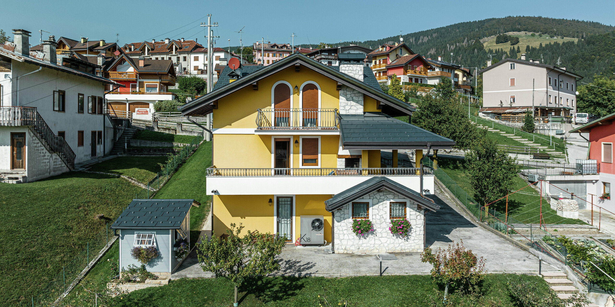 Maison individuelle à Gallio au charme alpin et toiture moderne en aluminium PREFA en P.10 gris sombre. Les panneaux de toiture durables PREFA R.16 offrent une protection optimale contre les intempéries et une apparence attrayante. La façade jaune à l'arrière du bâtiment a été combinée avec des éléments en pierre naturelle et des accents en bois - une symbiose parfaite avec l'environnement verdoyant. Le toit en aluminium de haute qualité est complété par le système de gouttière PREFA, qui assure un drainage fiable de l'eau. Un système de toiture élégant qui allie fonctionnalité et esthétique.