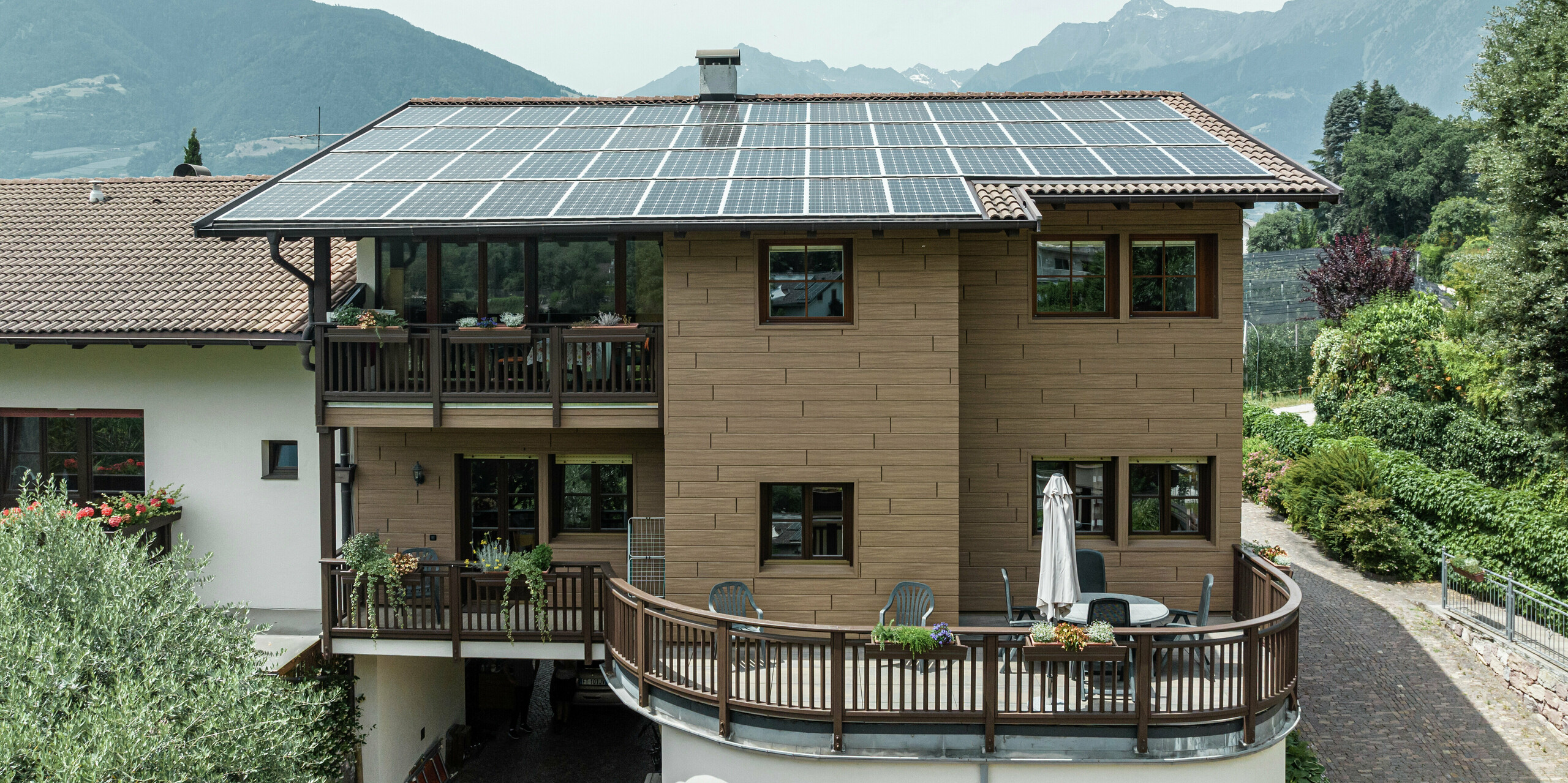 Appartements de vacances Prechtlhof rénovés à Merano, dans le Tyrol du Sud, avec Sidings PREFA en noyer foncé et une installation photovoltaïque à grande échelle sur le toit. La façade en aluminium à faible entretien et aspect bois allie durabilité et esthétique traditionnelle et s'intègre parfaitement dans le paysage alpin.