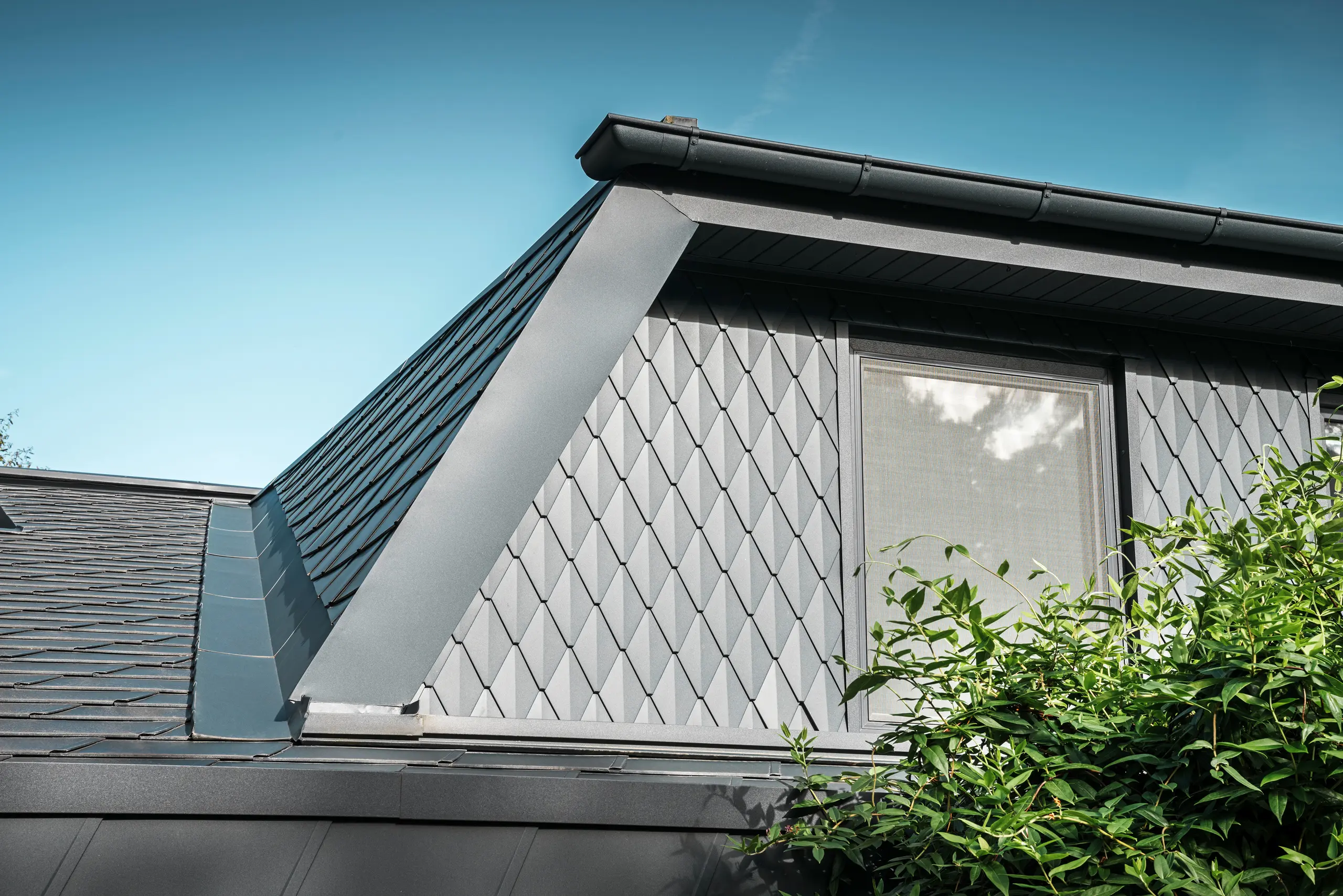 Lucarne trapézoïdale d'une maison individuelle à Mechernich, revêtue de petits losanges PREFA en P.10 anthracite. La toiture est recouverte de DS.19 PREFA de la même couleur. Le revêtement en aluminium de haute qualité garantit une résistance aux intempéries et un aspect moderne et esthétique.
