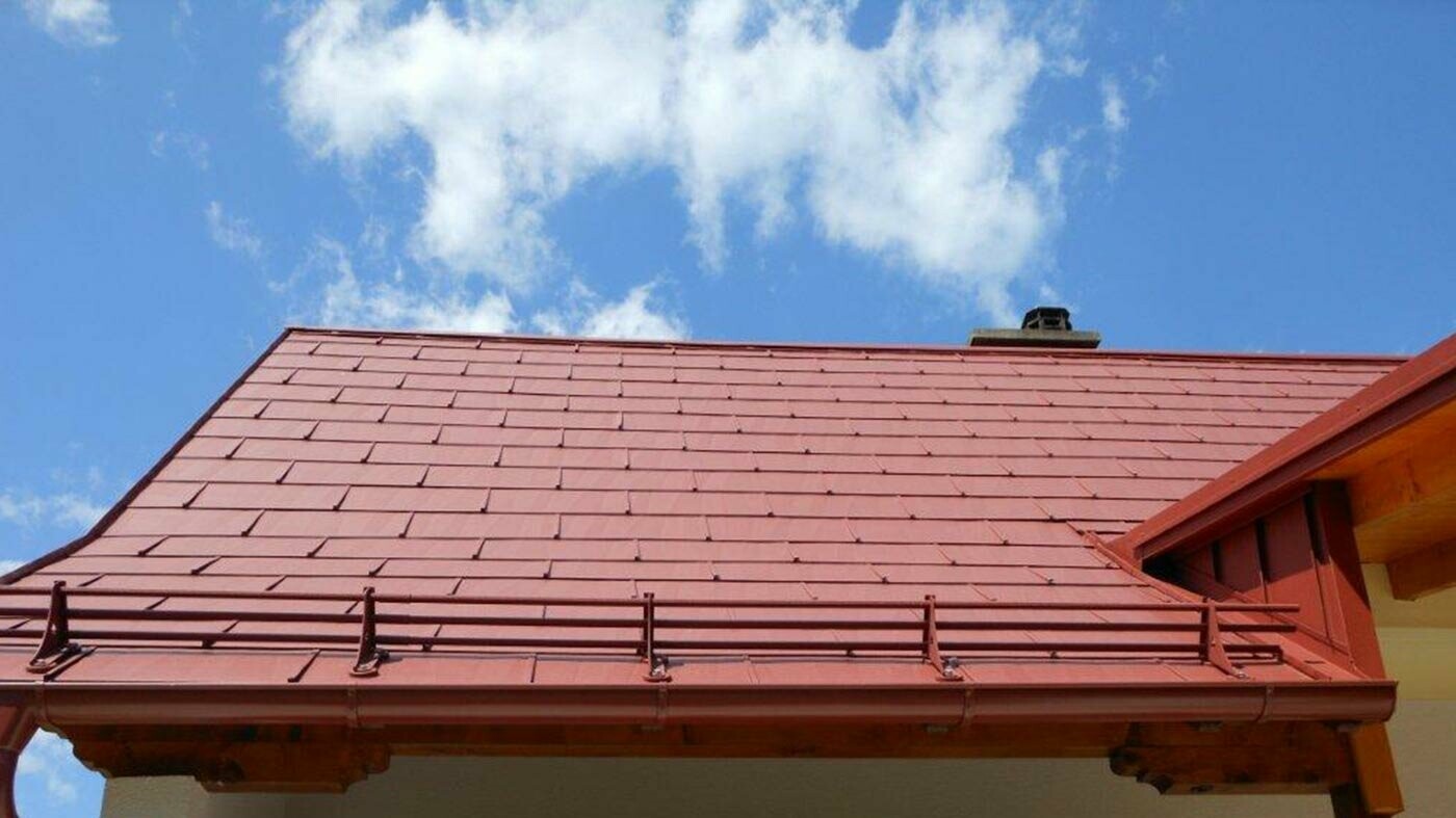 Vue détaillée d’une surface de toit composée de panneaux de toiture FX.12 PREFA couleur rouge oxyde et d’un système pare-neige.