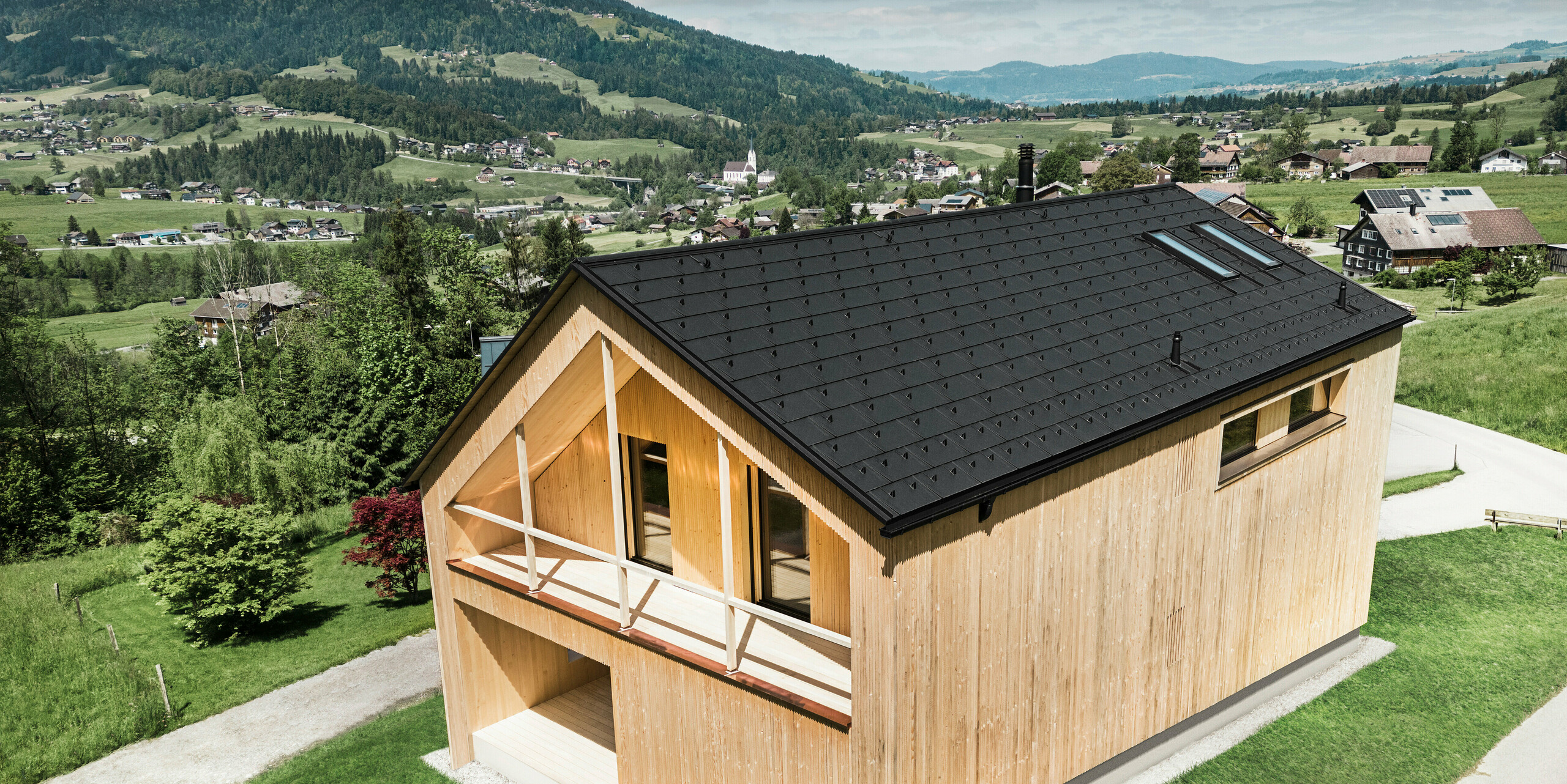 Maison individuelle dans la ville autrichienne d'Egg avec le panneau de toit solaire PREFA et le panneau de toit R.16 en noir, combinés à une façade en bois