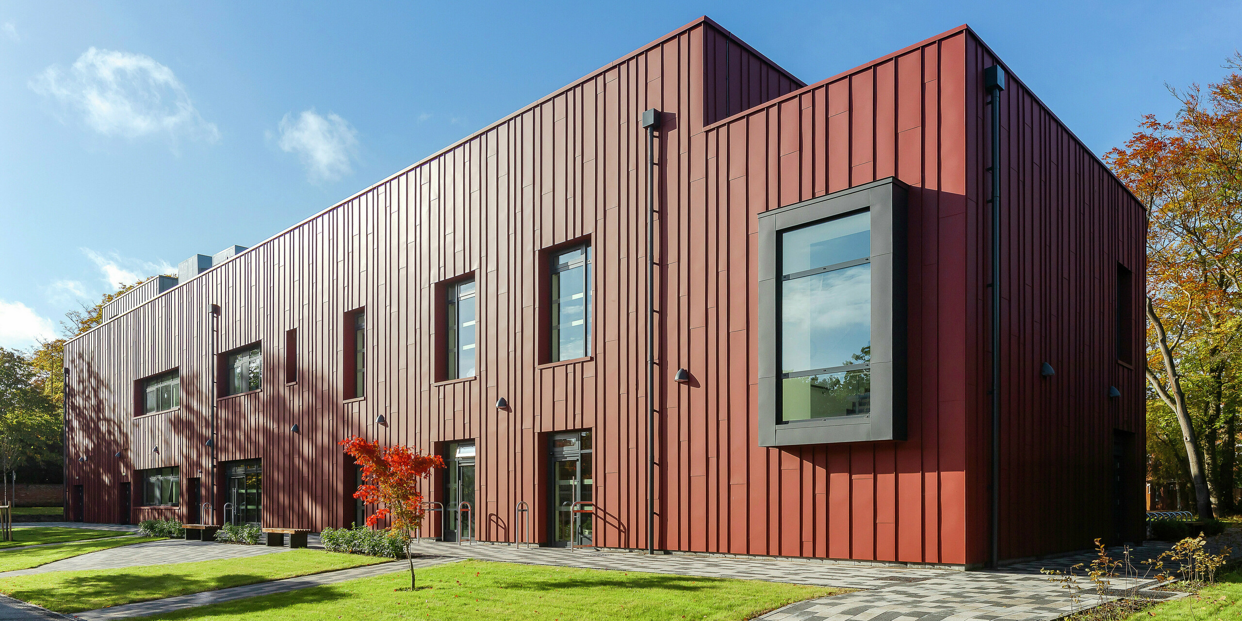 Une architecture moderne avec une façade robuste en aluminium : le Soldiers' Centre de Pirbright dispose d'un élégant toit à joint debout en PREFALZ en P.10 rouge oxyde, qui s'intègre harmonieusement dans l'environnement verdoyant. Les cadres de fenêtres en porte-à-faux remarquables en P.10 anthracite apportent des accents architecturaux. Le chemin pavé et l'espace vert bien entretenu soulignent le design accueillant du bâtiment. Construction durable et esthétique avec les produits en aluminium PREFA.