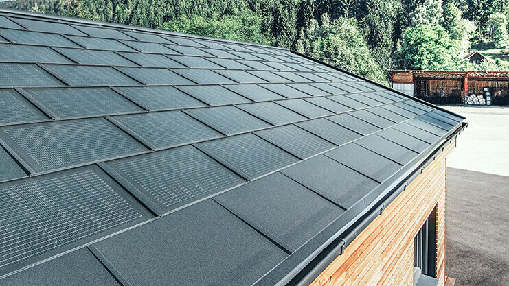 Tuile solaire PREFA en grand format, combinée avec le R.16 en noir, une gouttière carrée et une façade en bois de mélèze