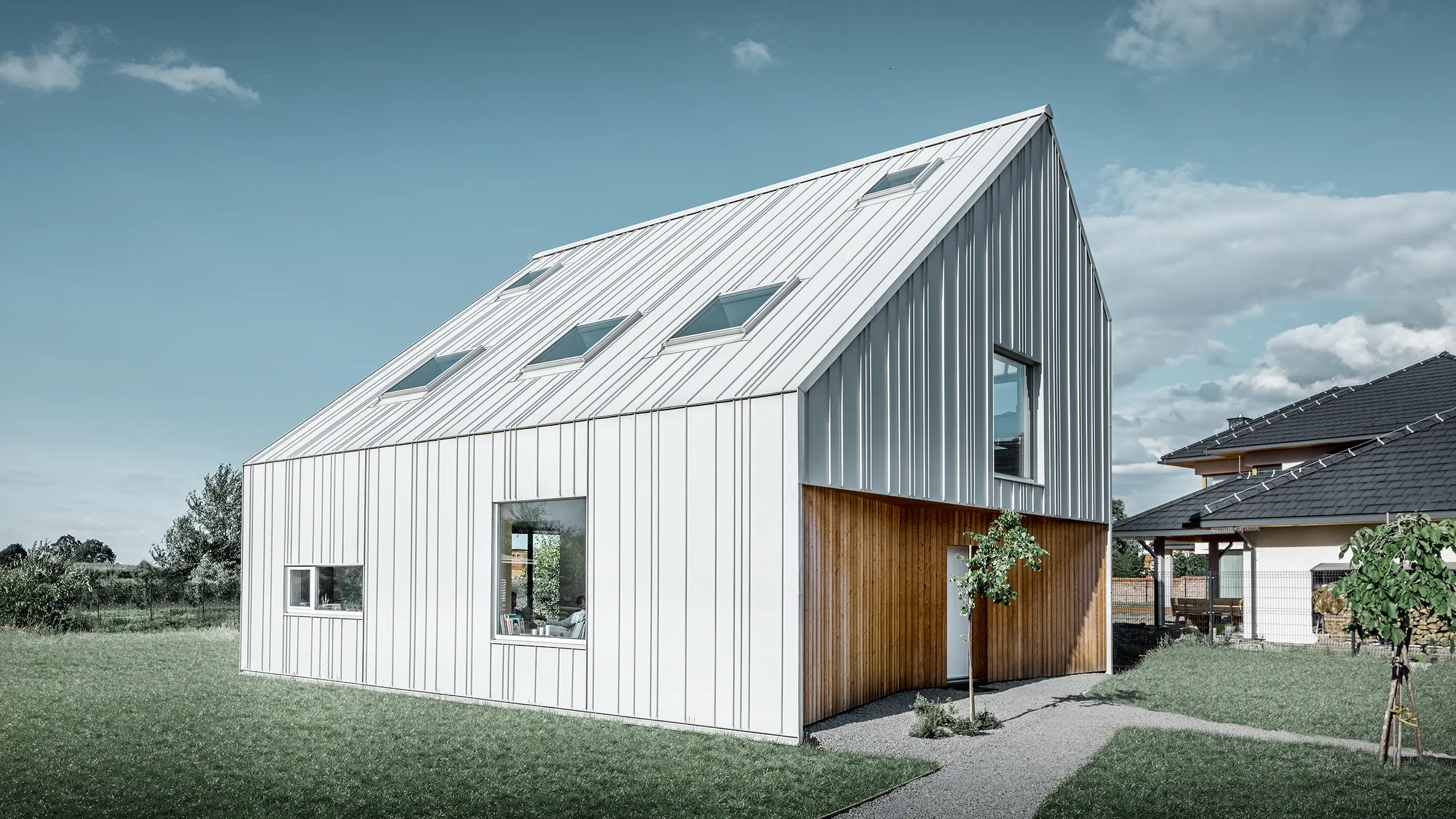 Maison individuelle moderne avec toit à pignon ; tout l’habillage extérieur a été réalisé avec PREFALZ en blanc Prefa. Les bacs de différentes largeurs s'étendent du toit à la façade. Plusieurs fenêtres de toit sont intégrées dans le toit.
