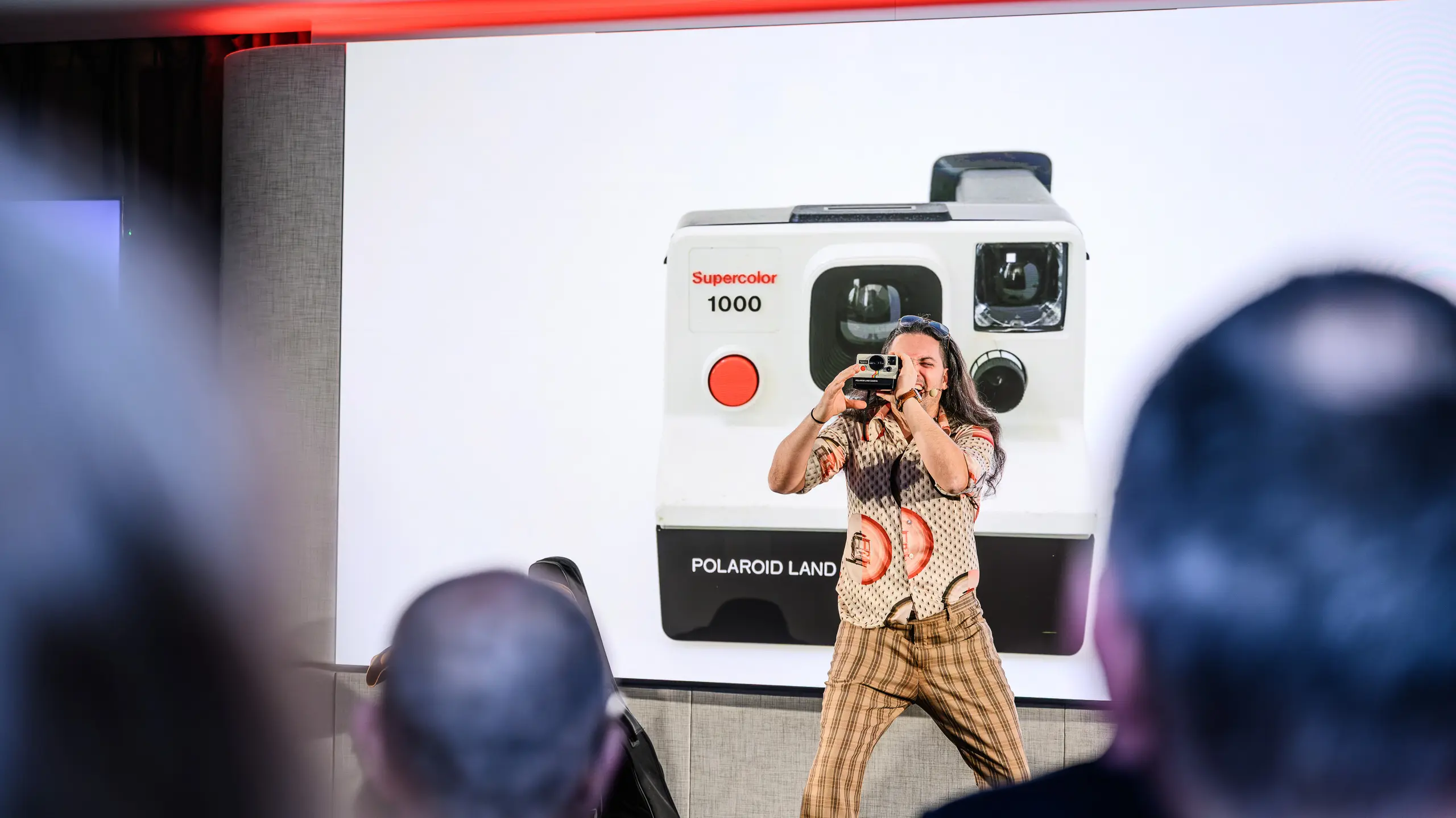 Un moment créatif lors de la présentation PREFARENZEN 2026 : le présentateur, plein d’humour, immortalise l’événement avec un appareil photo Polaroid rétro, devant une projection géante de l’emblématique Supercolor 1000. Cette contribution artistique fait le lien entre passé et futur, à l’image de PREFA et de ses produits en aluminium durable. Une soirée riche en émotions, en innovation et en inspiration esthétique.