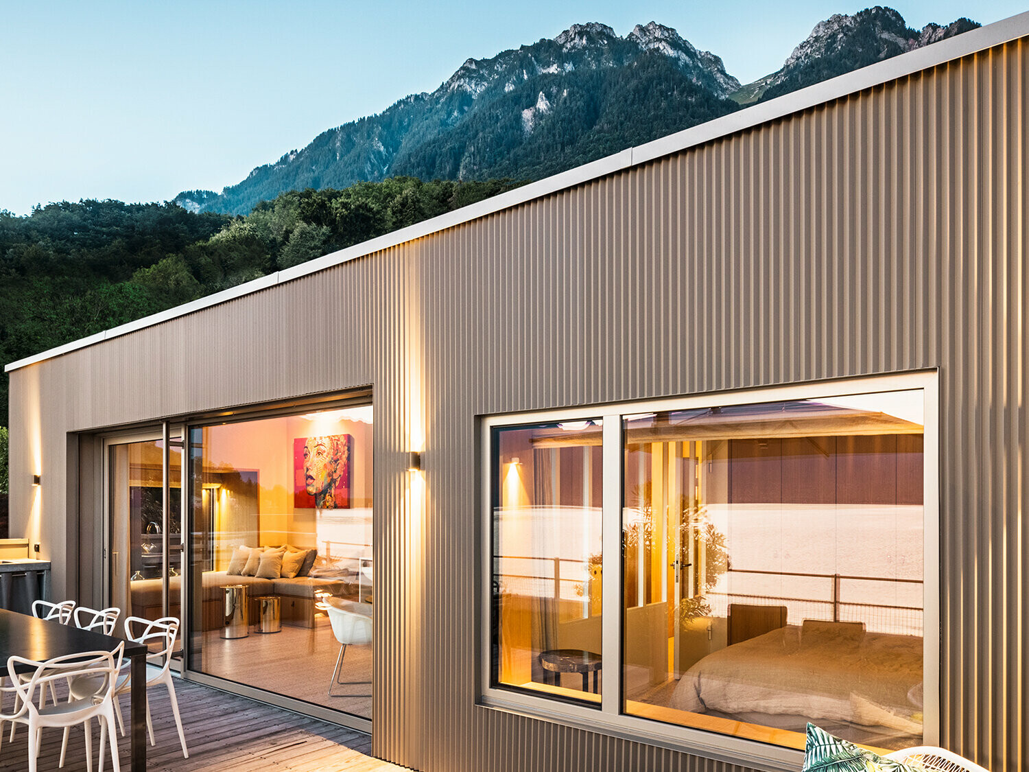 Vue sur la terrasse et une partie de l'intérieur du bâtiment le soir.