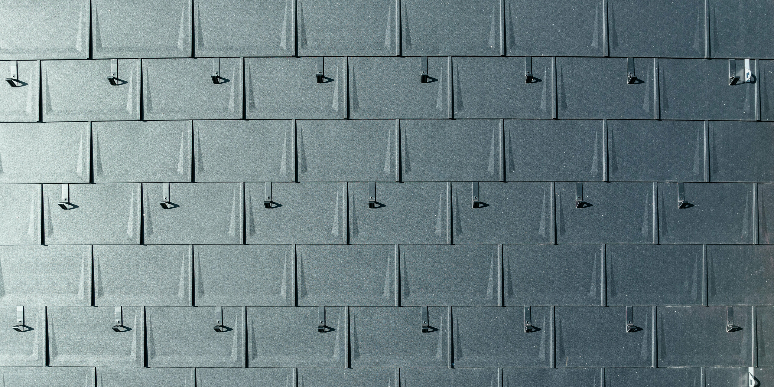 Gros plan d'une couverture de toit en aluminium PREFA. Les R.16 PREFA dans la couleur populaire P.10 anthracite sont reliés entre eux avec précision. Les panneaux en aluminium de haute qualité offrent une solution de toiture durable, résistante aux intempéries et visuellement attrayante. Les butées à neige offrent une sécurité supplémentaire.