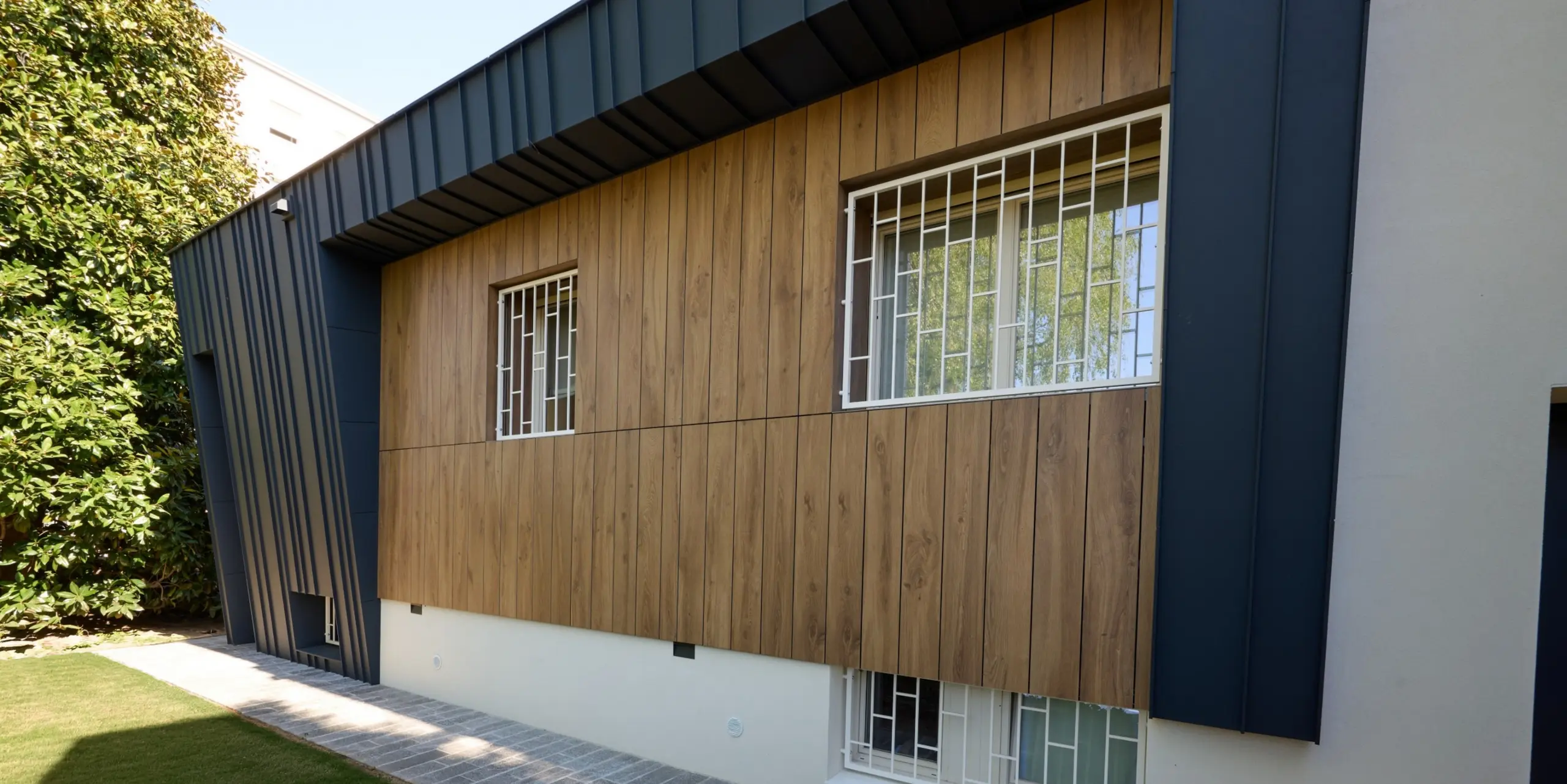 Vue détaillée de la Villa Castellanza, avec sa remarquable façade PREFALZ en aluminium anthracite P.10 et ses surfaces en bois chaleureux. Les joints debout précis encadrent élégamment les fenêtres et confèrent à l'enveloppe du bâtiment un effet tridimensionnel moderne. L'aluminium PREFA impressionne par sa durabilité, sa résistance aux intempéries et sa haute qualité architecturale, alliant harmonieusement design et fonctionnalité.