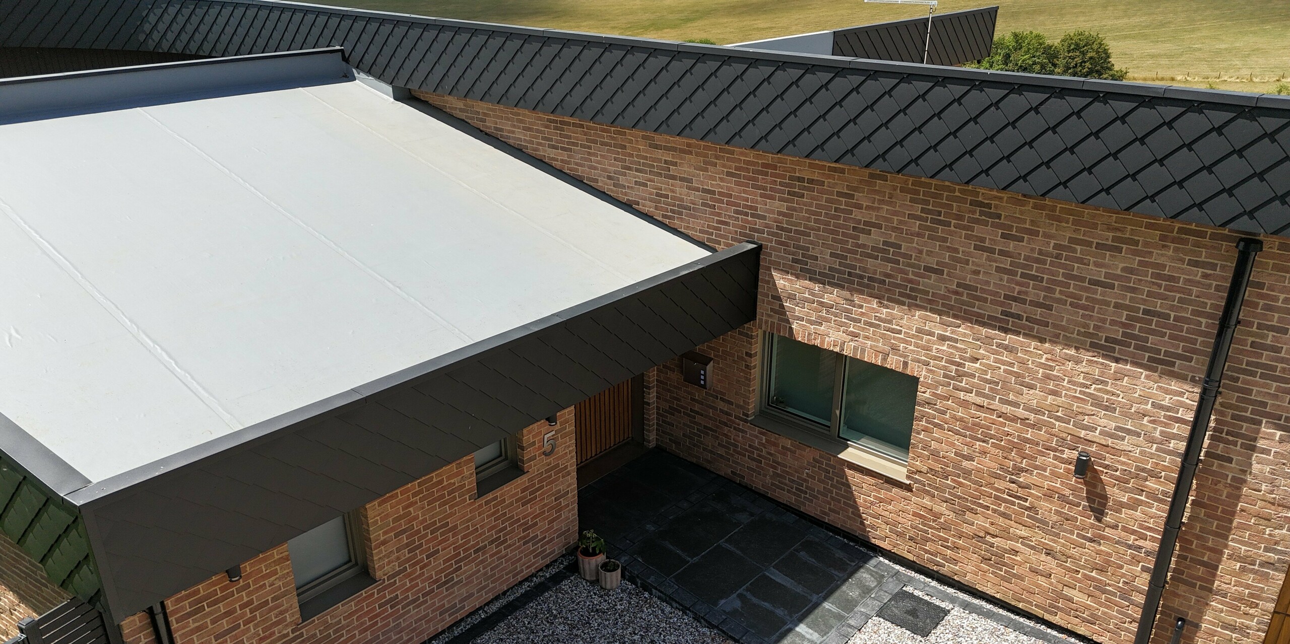 Cette maison individuelle moderne séduit par son auvent d'entrée remarquable et l'élégante combinaison d'une façade en briques et de losanges de façade PREFA 20 x 20 en P.10 anthracite. La robustesse des panneaux métalliques souligne la qualité architecturale du bâtiment. Grâce à la qualité des produits en aluminium PREFA, la façade résiste aux intempéries et est facile d'entretien. L'alliance des matériaux naturels et des solutions modernes en aluminium fait de cette propriété un modèle d'habitat durable et élégant.