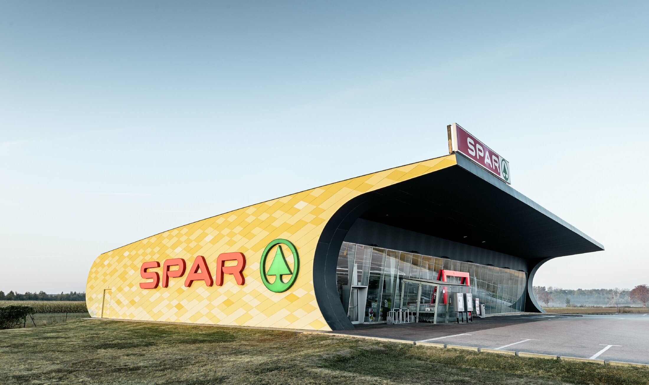 Magasin Spar — Façade en aluminium PREFA habillée de losanges jaune pâle à orange et arborant le logo Spar