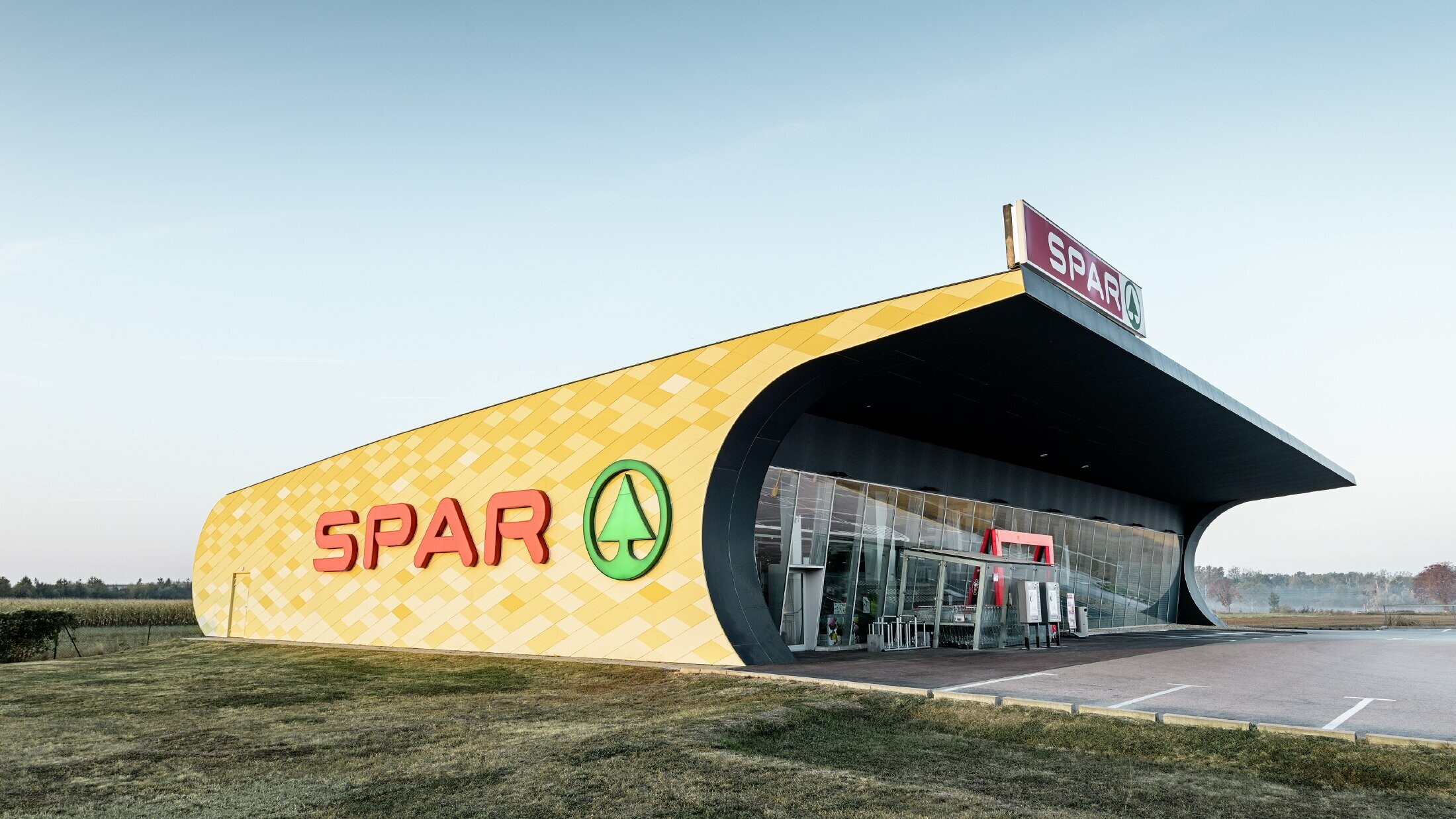 Magasin Spar — Façade en aluminium PREFA habillée de losanges jaune pâle à orange et arborant le logo Spar