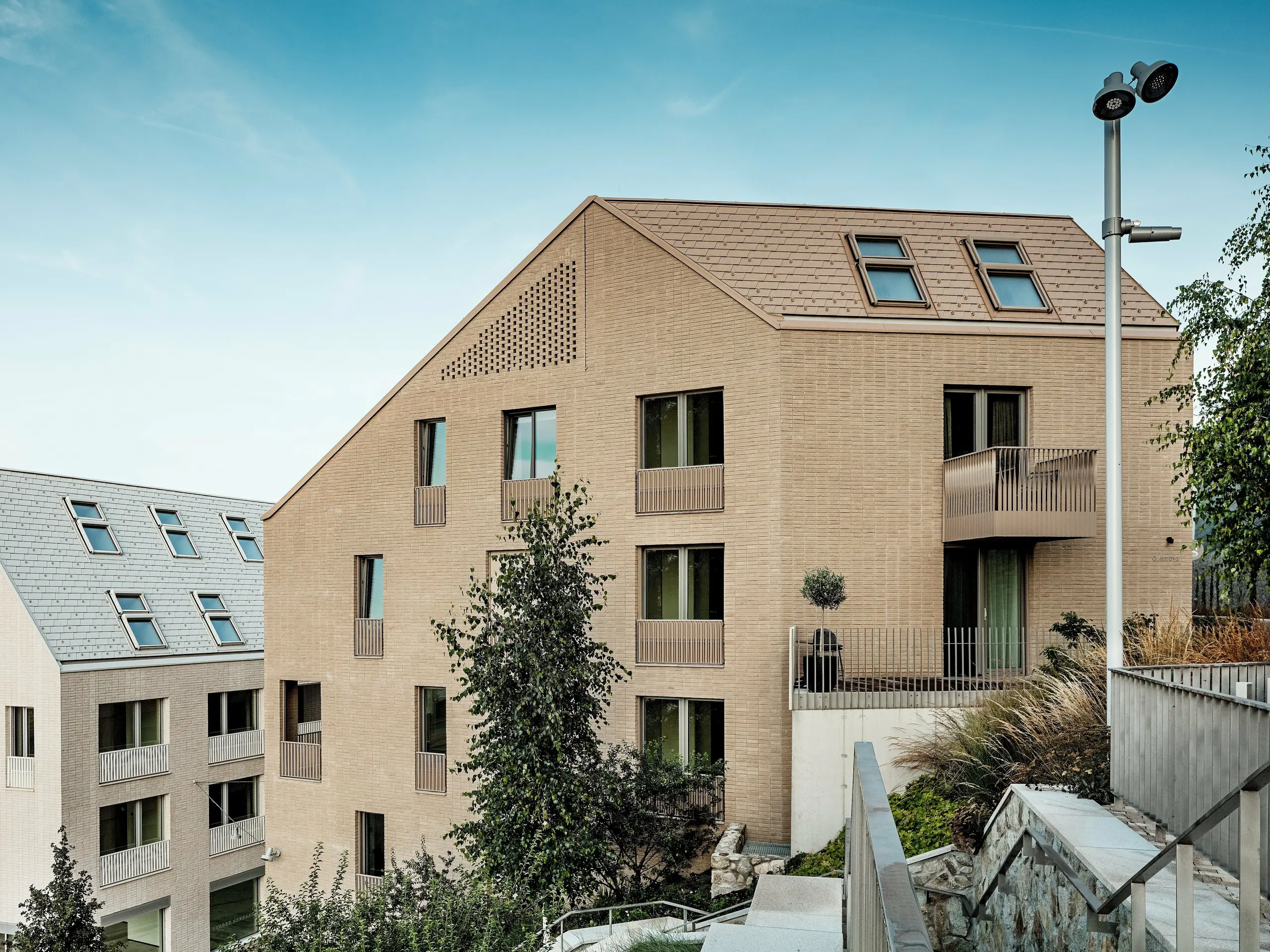 Les immeubles résidentiels modernes du quartier Vydrica à Bratislava se caractérisent par un design épuré et minimaliste, et une intégration harmonieuse à la topographie. Les toitures à forte pente, revêtues de tuiles en aluminium PREFA P.10 Brun Sable et Blanc Prefa, posées avec précision, créent des contrastes visuels saisissants grâce à leurs surfaces texturées et leurs puits de lumière intégrés. L'harmonie entre la toiture et la façade confère aux surfaces un aspect sobre et raffiné. L'aluminium PREFA est reconnu pour sa durabilité, sa facilité de pose, sa grande résistance aux intempéries et permet la réalisation de solutions de toiture sophistiquées et durables.