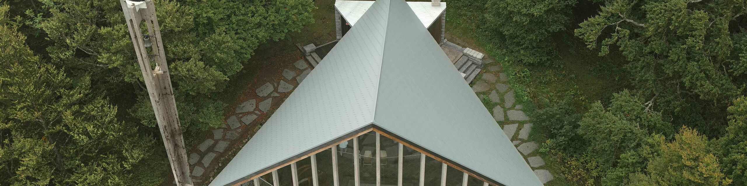 Prise de vue par drone de la toiture de la chapelle du Col de la Schlucht rénovée grâce aux bardeaux en aluminium PREFA dans la teinte P.10 gris souris. On aperçoit également les larges baies vitrées sur le devant de la chapelle.