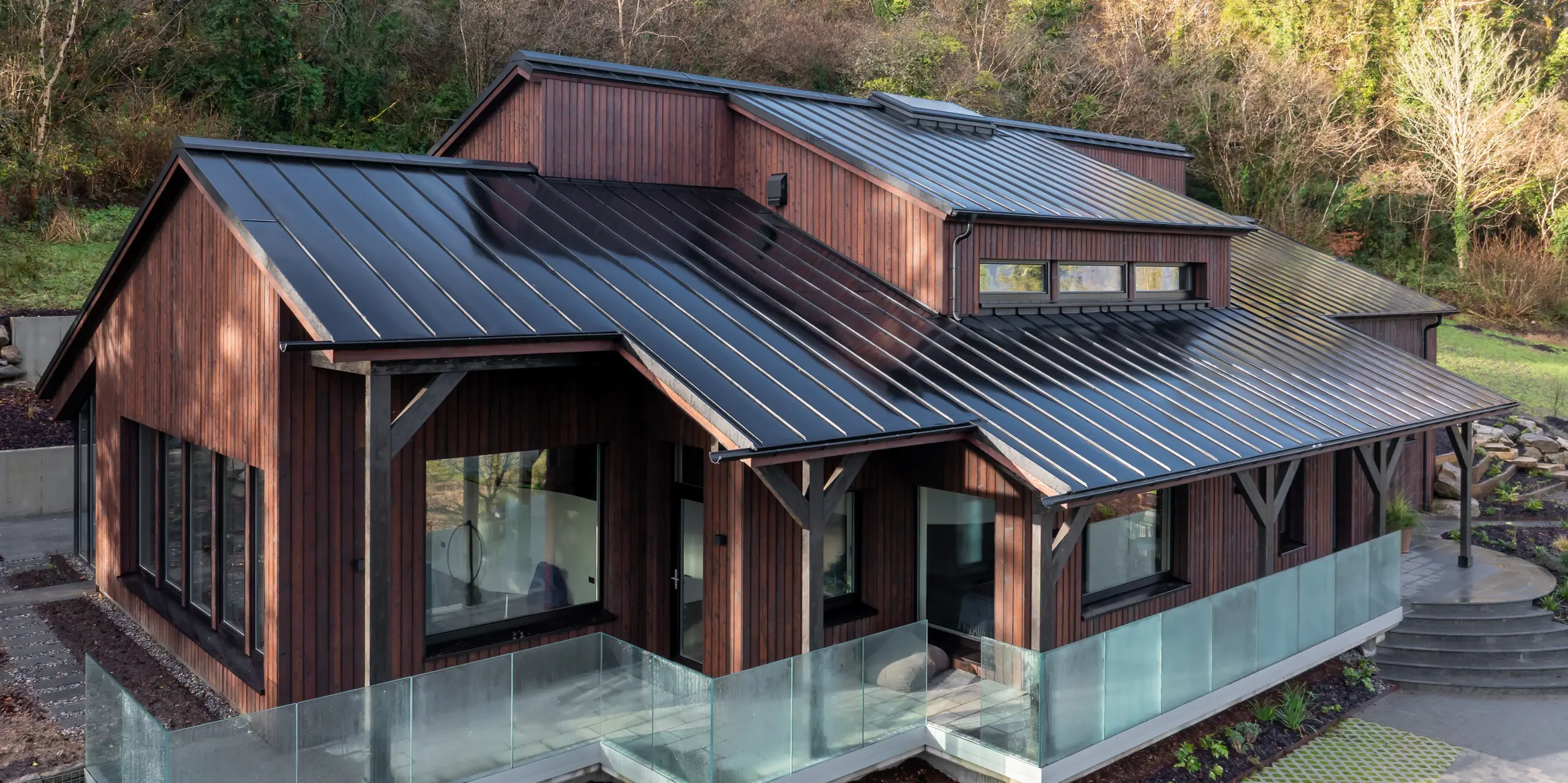 Vue oblique de la Maison Holywell à Sligo : la perspective suit les pentes du toit, où la toiture en aluminium PREFALZ P.10 Noir révèle avec élégance sa structure à joints debout. Les lignes épurées s’étendent avec dynamisme sur plusieurs niveaux, attirant le regard vers la partie surélevée du toit et sa lucarne. La surface légèrement réfléchissante souligne la qualité de la réalisation et crée une élégante impression de profondeur. L’aluminium PREFA se distingue par sa durabilité, sa résistance à la corrosion et sa protection fiable même dans les climats les plus exigeants.