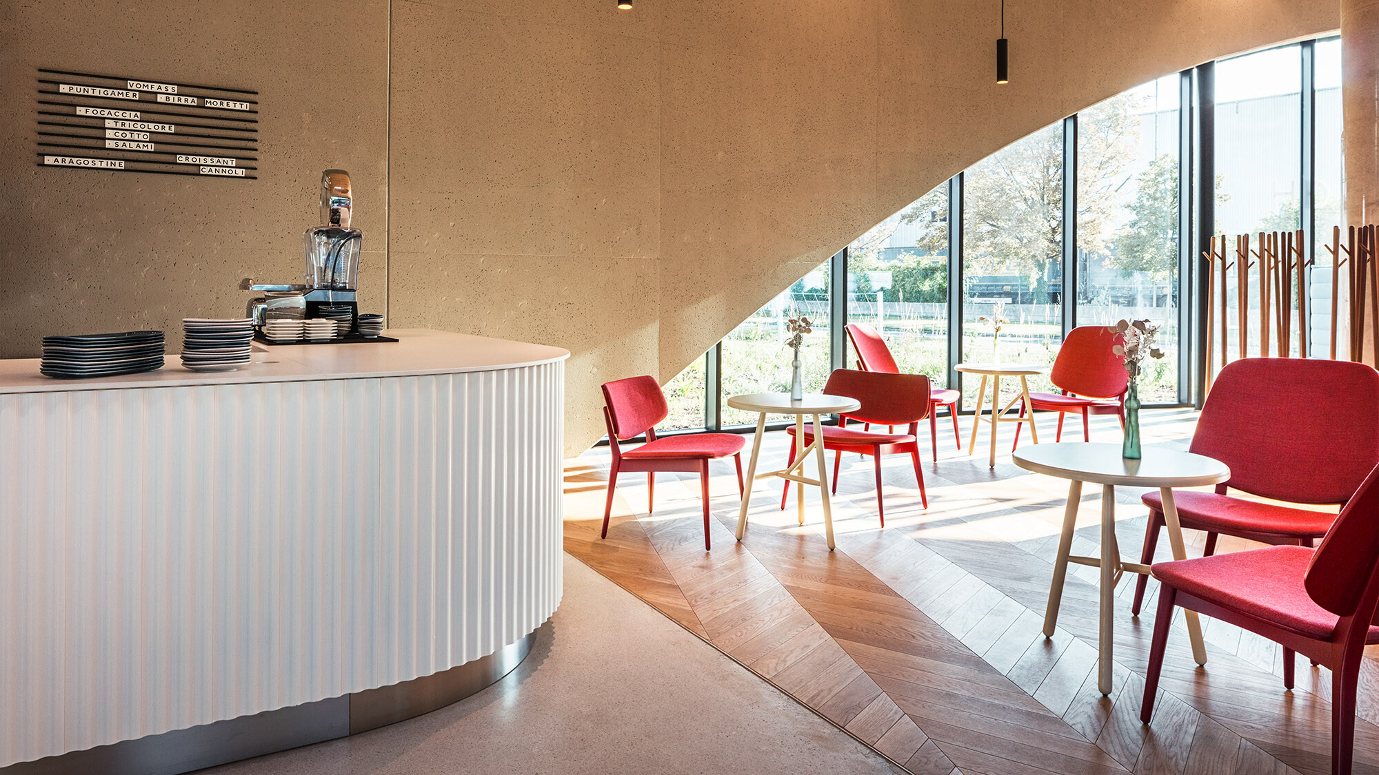 Une des salles du restaurant avec un comptoir, des chaises rouges et un sol en parquet, derrière lequel on peut voir une des fenêtres en arc de cercle.