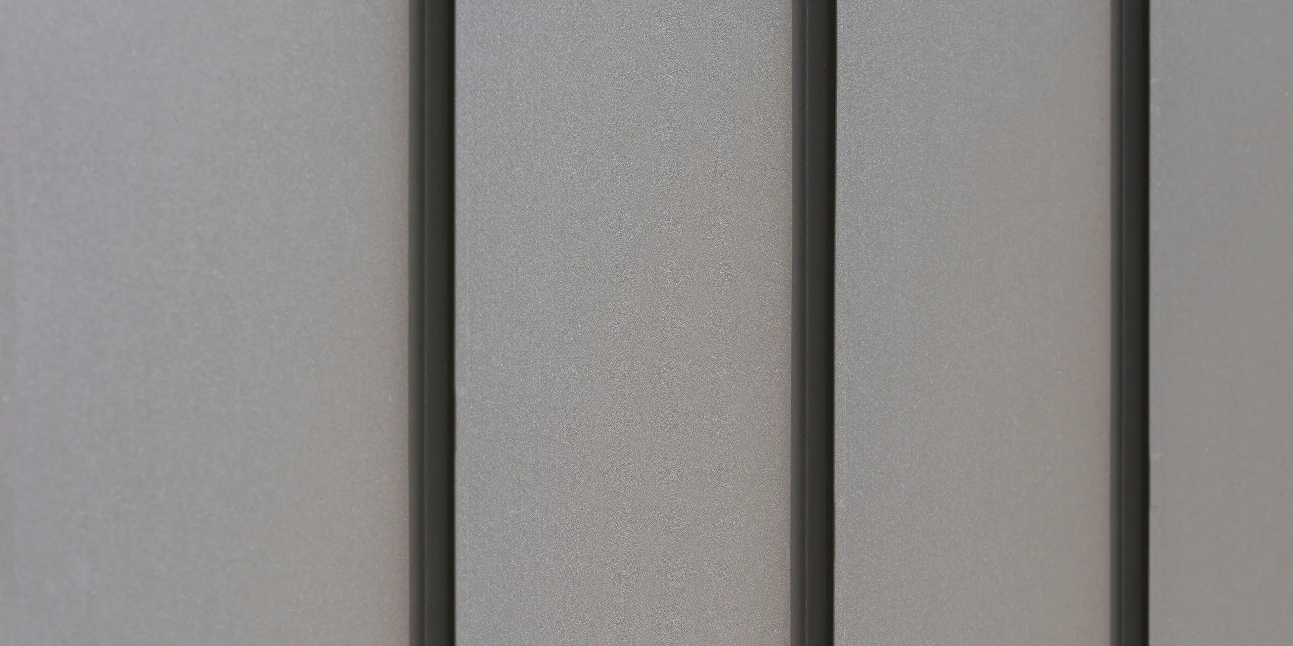 Gros plan d'un revêtement de façade moderne en aluminium avec des bacs verticaux créant un motif esthétiquement texturé. L'aluminium provient de PREFA Aluminium Products GmbH.
