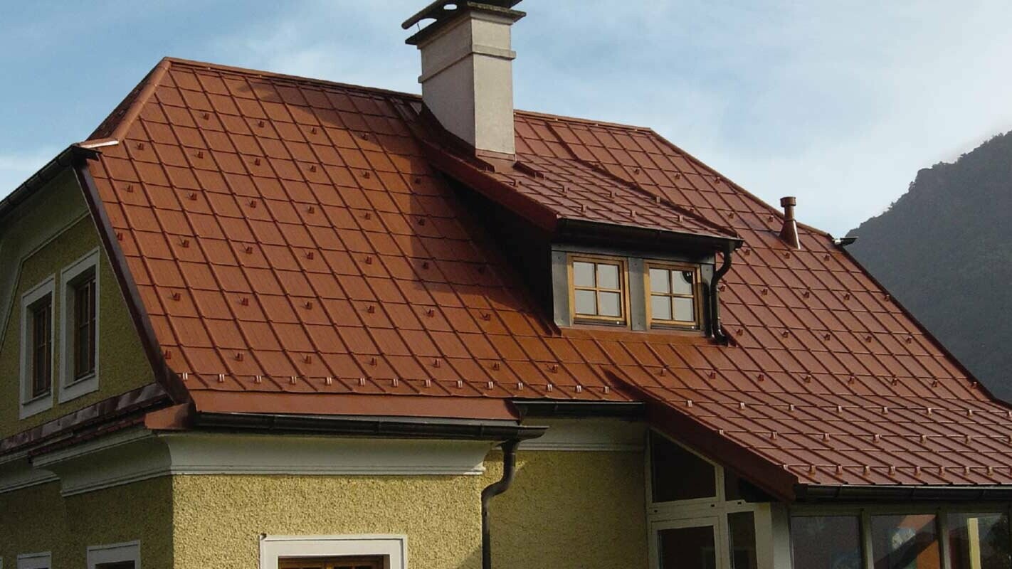 Maison individuelle avec toiture à deux pans en croupe et lucarne, fraîchement rénovée à l’aide de tuiles PREFA couleur rouge tuile