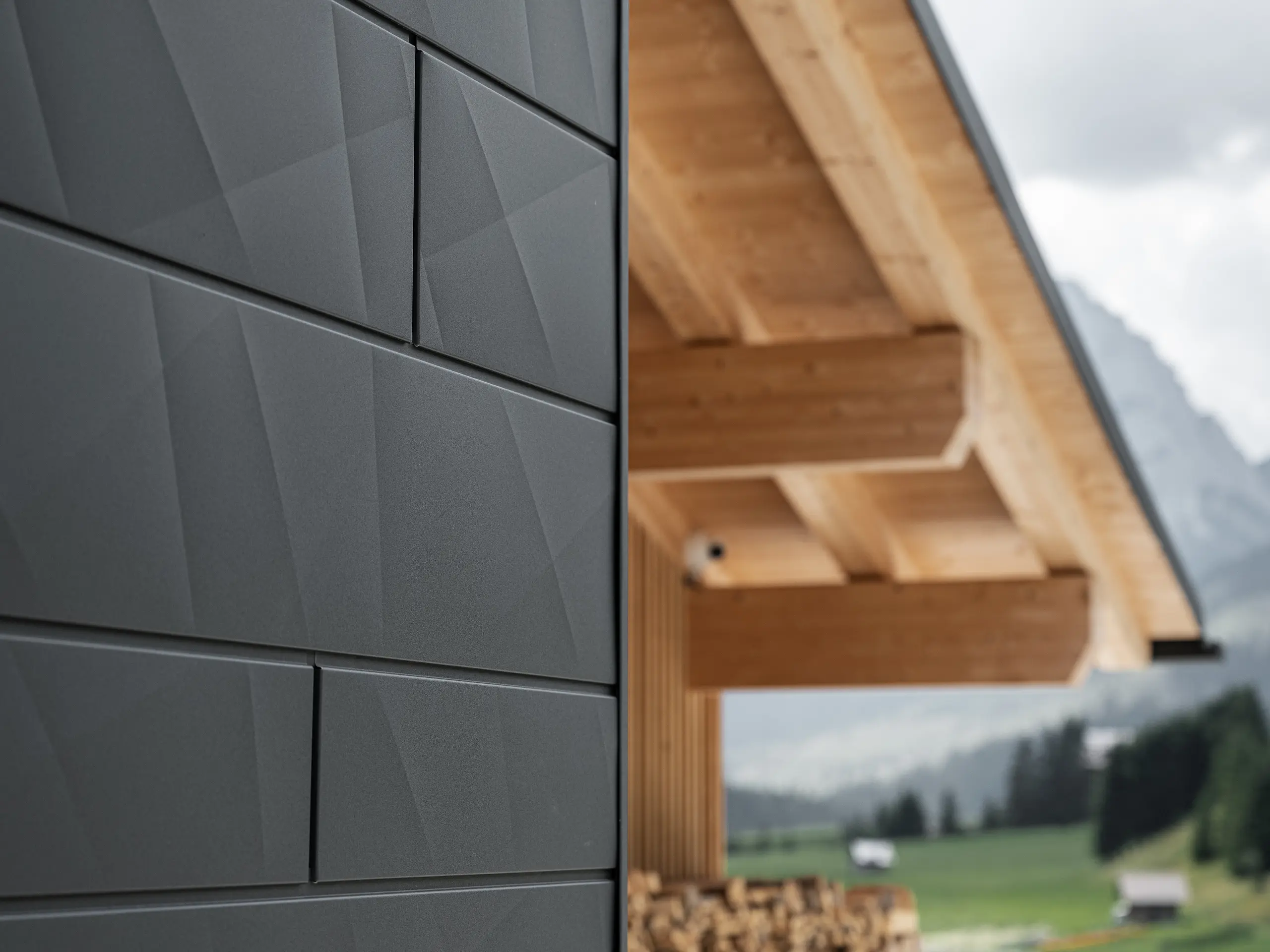 Gros plan sur les panneaux de façade Siding.X en P.10 noir de PREFA à la Casa Hoffe à Sappada, Italie. Le système de façade en aluminium au design moderne et abstrait, crée un contraste intéressant avec les éléments apparents de la charpente en bois. Cette solution de façade innovante, qui s'intègre harmonieusement à l'environnement alpin, combine fonctionnalité, durabilité et culture architecturale esthétique.