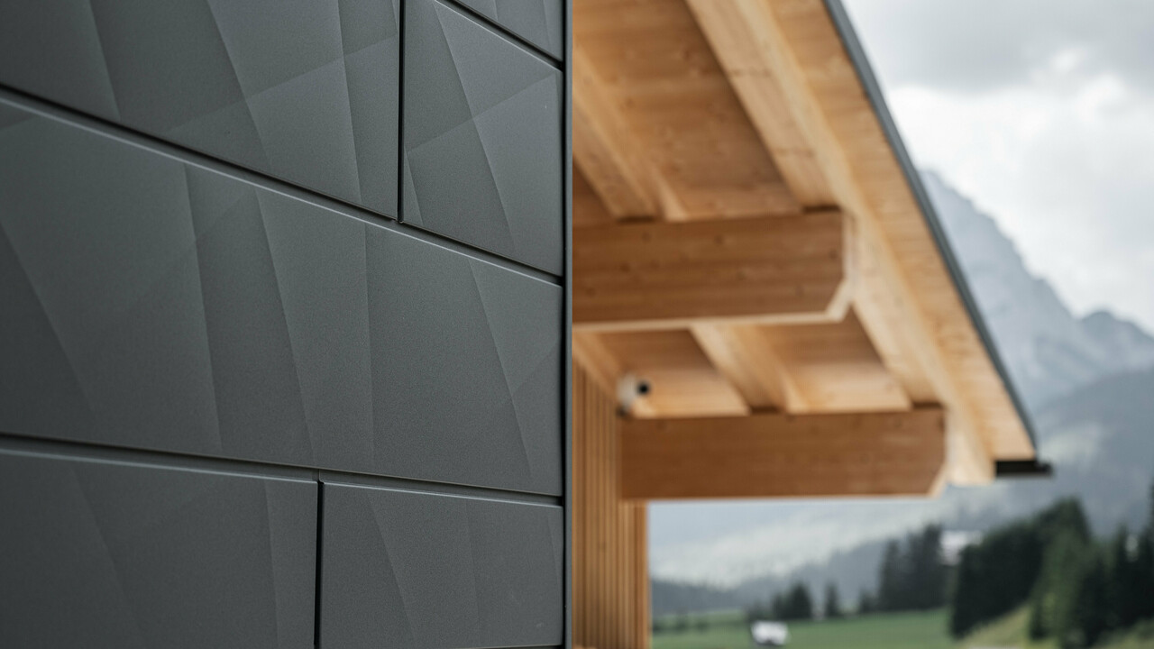 Gros plan sur les panneaux de façade Siding.X en P.10 noir de PREFA à la Casa Hoffe à Sappada, Italie. Le système de façade en aluminium au design moderne et abstrait, crée un contraste intéressant avec les éléments apparents de la charpente en bois. Cette solution de façade innovante, qui s'intègre harmonieusement à l'environnement alpin, combine fonctionnalité, durabilité et culture architecturale esthétique.