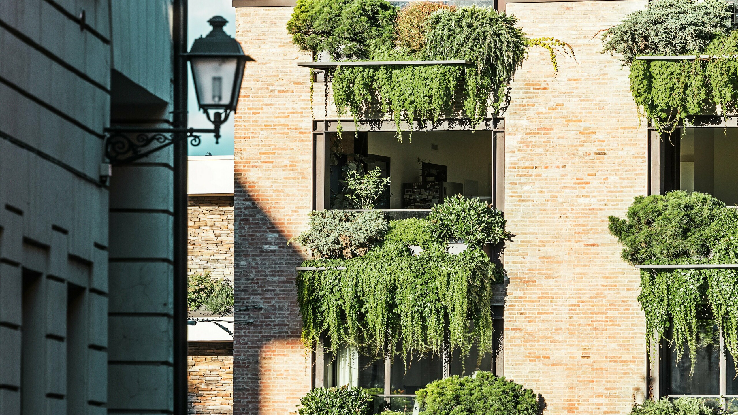 Vue détaillée d'une façade en briques végétalisée en Italie avec des jardins suspendus, des détails architecturaux PREFALZ et la vieille ville adjacente avec ses lanternes.