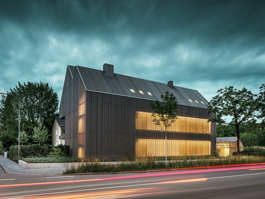 L'immeuble résidentiel de Dachau au crépuscule. Nous apercevons la lumière depuis l'intérieur du bâtiment aux travers la façade semi-perforée, ce qui donne à l'ensemble un style inhabituel.