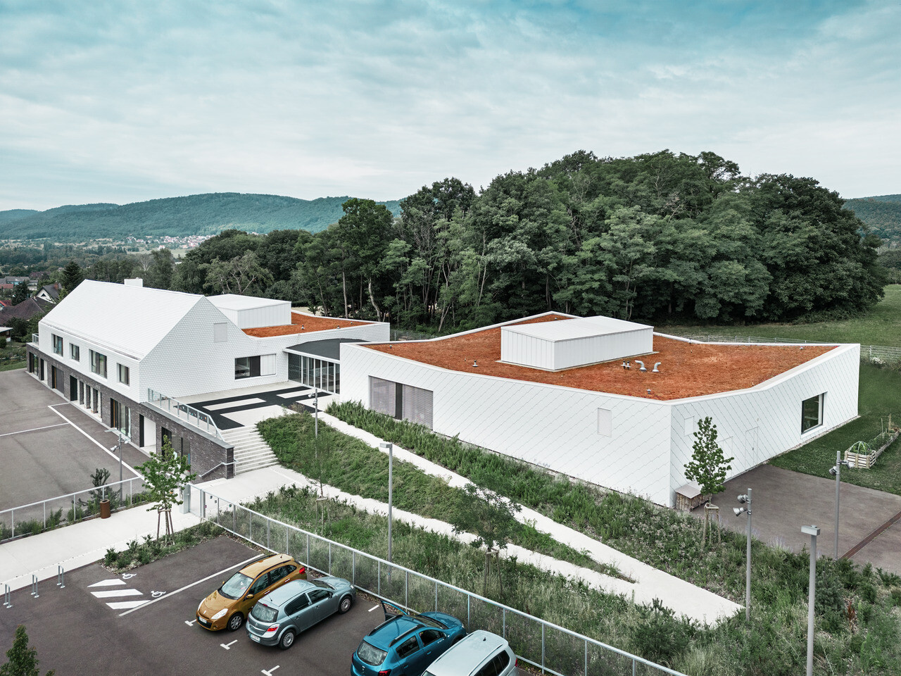 Prise de vue éloignée et d'ensemble du centre scolaire d'Otterswiller dont la façade a été habillée avec les losanges 44x44 Prefa dans la teinte P.10 blanc Prefa.