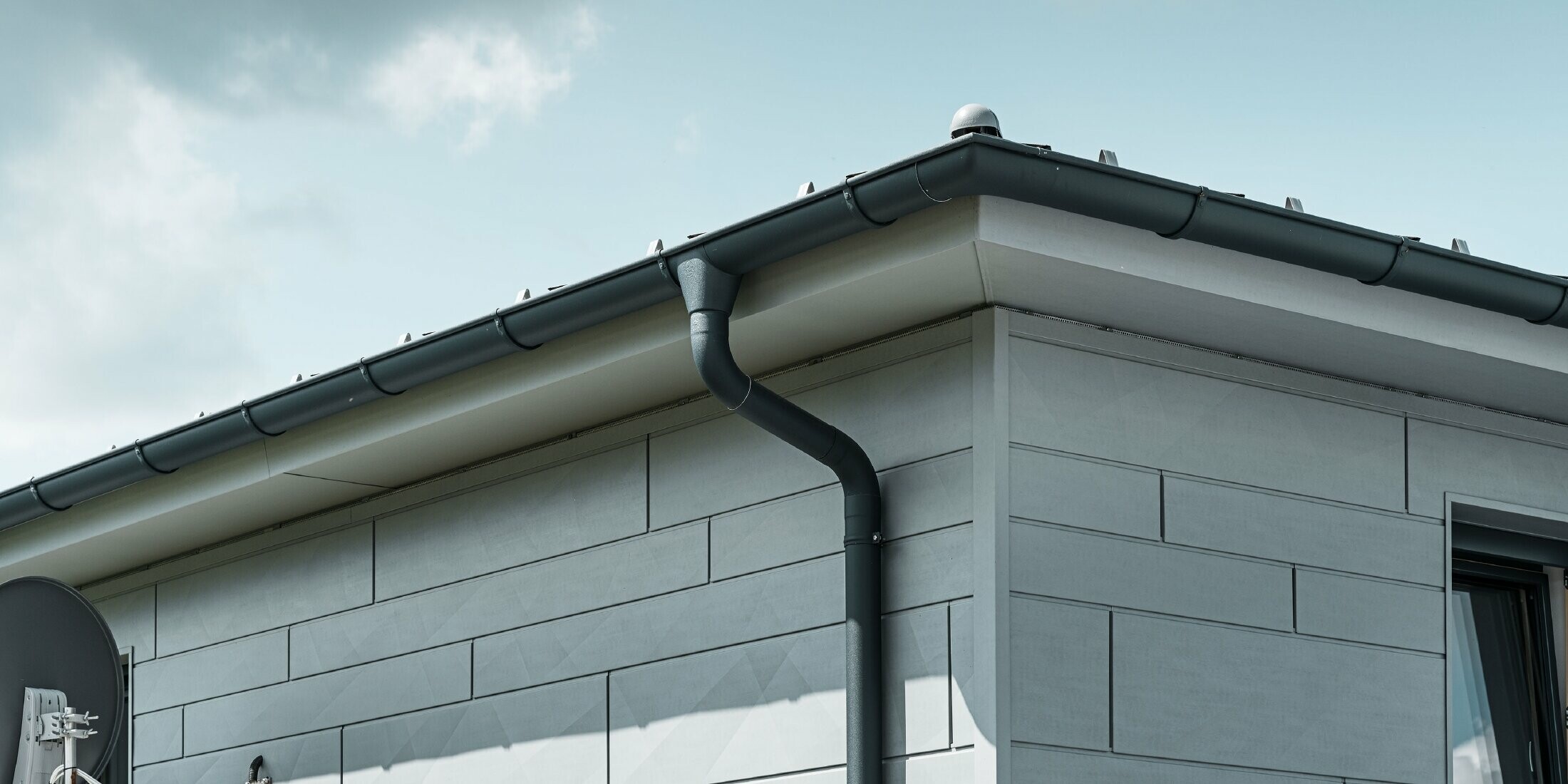 Sous-face de toiture avec gouttière, naissance de gouttière et tuyau de descente PREFA couleur anthracite avec façade de Siding.X PREFA couleur gris quartz