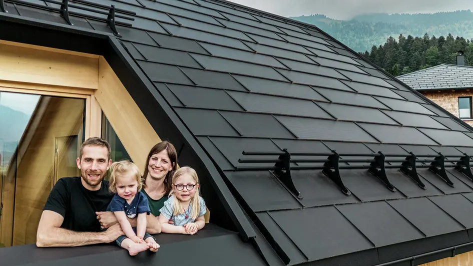 Les deux maîtres d'ouvrage et leurs enfants profitent de la vue depuis la loggia de leur maison neuve, équipée d'élégantes tuiles solaires PREFA en P.10 noir.