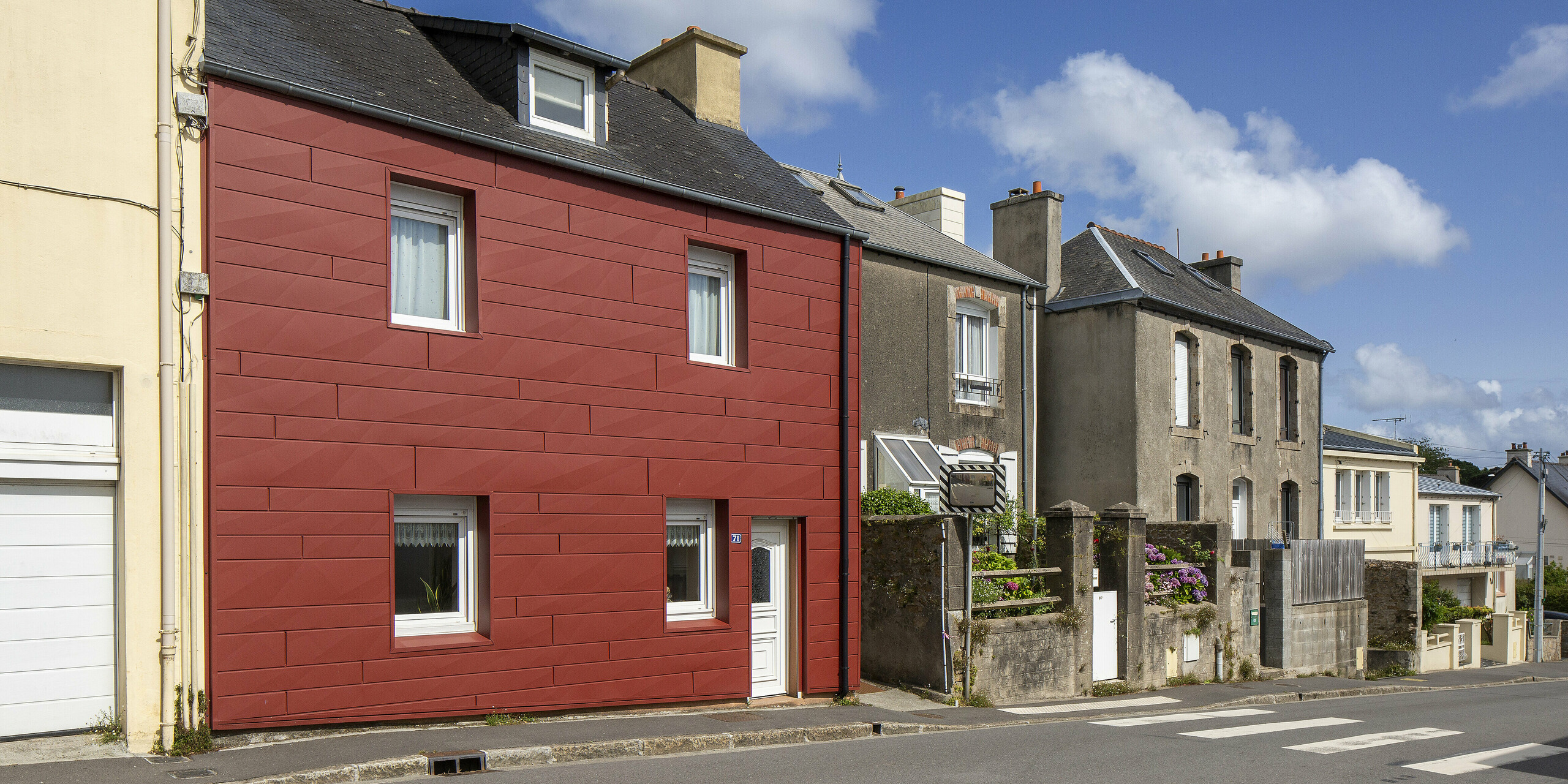 Parmi les façades traditionnelles, le projet de référence PREFA, avec ses panneaux Siding.X en rouge oxyde, attire immédiatement le regard. La pureté des lignes et la texture de la surface créent un contraste saisissant avec l'architecture environnante. Une rénovation réussie qui allie design, qualité et fonctionnalité : durable, facile d'entretien et d'une originalité architecturale remarquable.