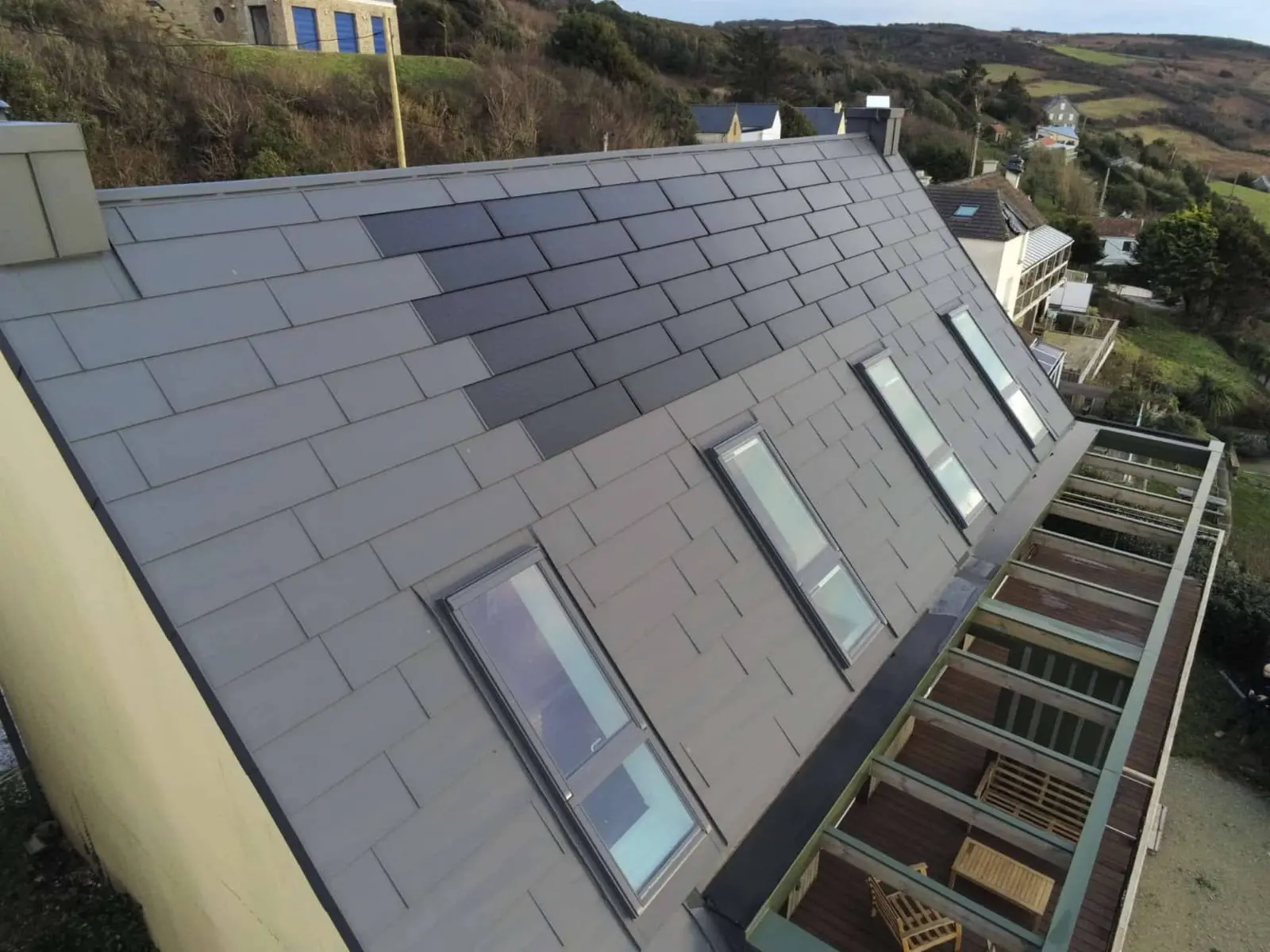 Vue latérale depuis la toiture de cette maison individuelle située face à la mer, à Les Pieux. Elle a récemment été rénovée avec les produits de toiture PREFA : panneaux FX.12 et tuile solaire PREFA dans la teinte P.10 gris sombre.