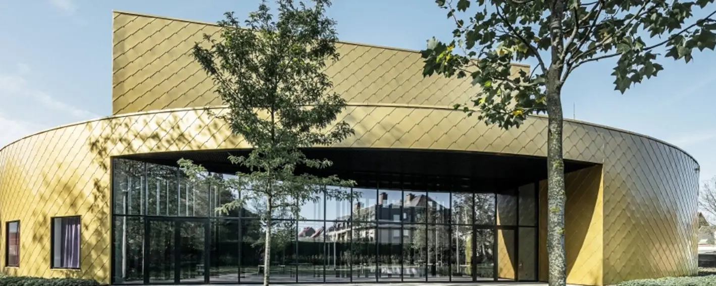 Vue de face du centre culturel. Le bâtiment est revêtu de losanges 44x44 PREFA dans les teintes maya gold et noir P.10