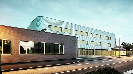 Vue du soir du collège Léontine Dolivet à Cesson-Sévigné. Au premier plan, une rue bien délimitée longe un immeuble bas aux larges baies vitrées. Derrière, se dresse le bâtiment principal, dont la façade incurvée en aluminium, composée de losanges PREFA argent métallisé, scintille sous la douce lumière. Plusieurs fenêtres rectangulaires et une clôture claire structurent la composition. La scène est éclairée par les lampadaires, et le ciel d'un bleu frais offre un spectacle moderne et élégant.