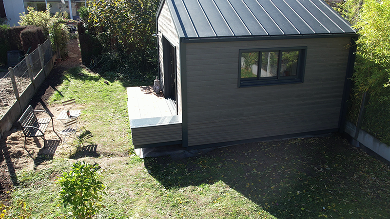Vue éloignée et surélevée de cette maison dont la couverture a été réalisé en joint debout en aluminium PREFA. Sur le côté gauche de la photo, on peut voir un jardin potager. 