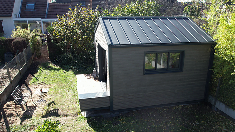 Vue éloignée et surélevée de cette maison dont la couverture a été réalisé en joint debout en aluminium PREFA. Sur le côté gauche de la photo, on peut voir un jardin potager. 